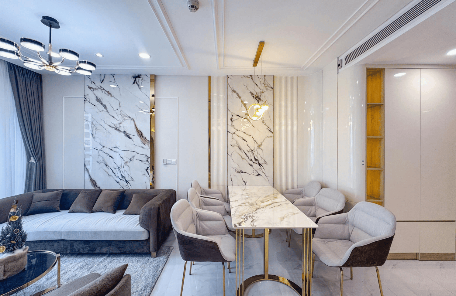 Modern living and dining area with marble wall panels, soft gray seating, and contemporary ceiling lighting in a cohesive open layout.