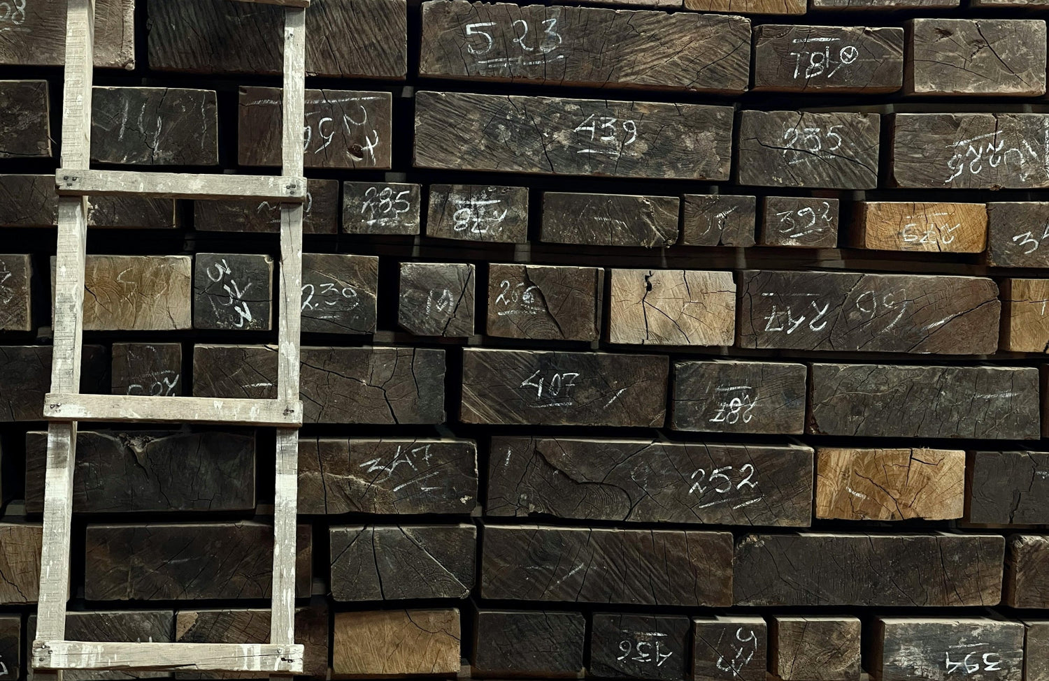 Stacked wooden beams marked with white numbers, showcasing natural grain patterns and weathered textures, alongside a rustic wooden ladder.