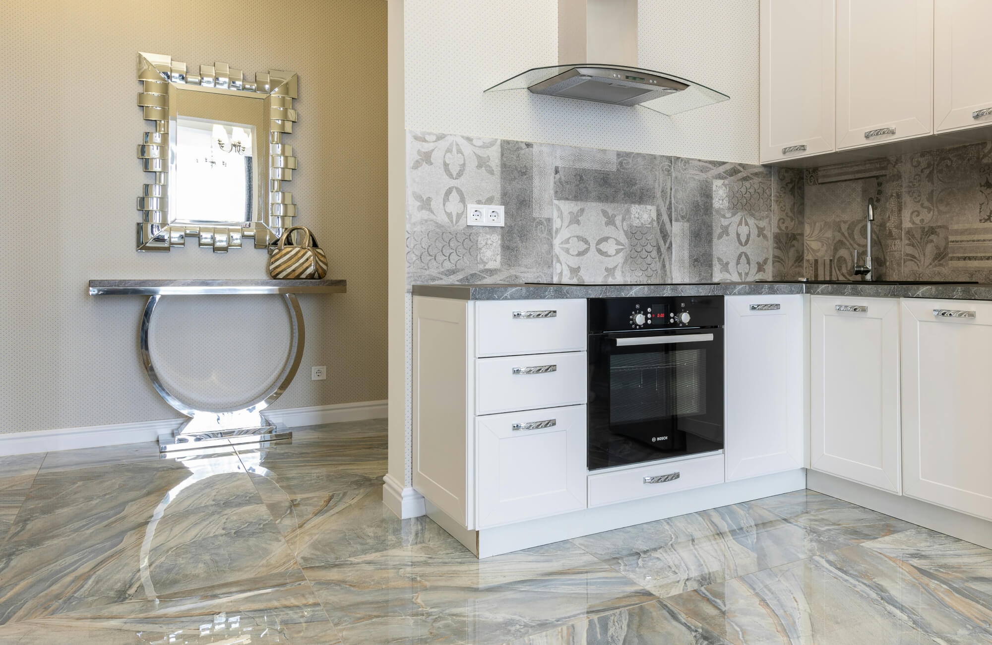 Luxurious kitchen with glossy marble-look flooring and patterned gray backsplash tiles, complementing the sleek white cabinetry