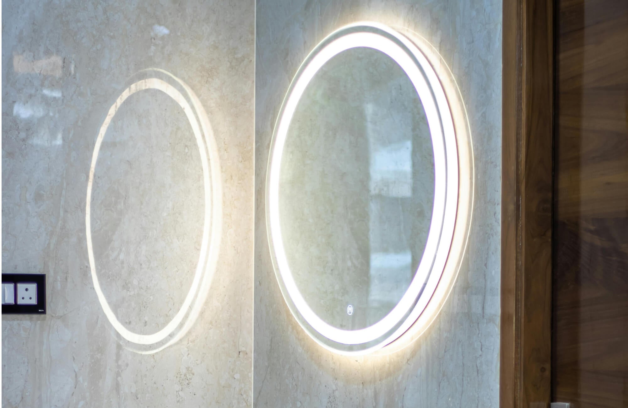 Modern bathroom wall showcasing an oval LED bathroom mirror with a bright halo-style light, casting a soft glow against textured stone surfaces for a clean, contemporary, and spa-inspired aesthetic.