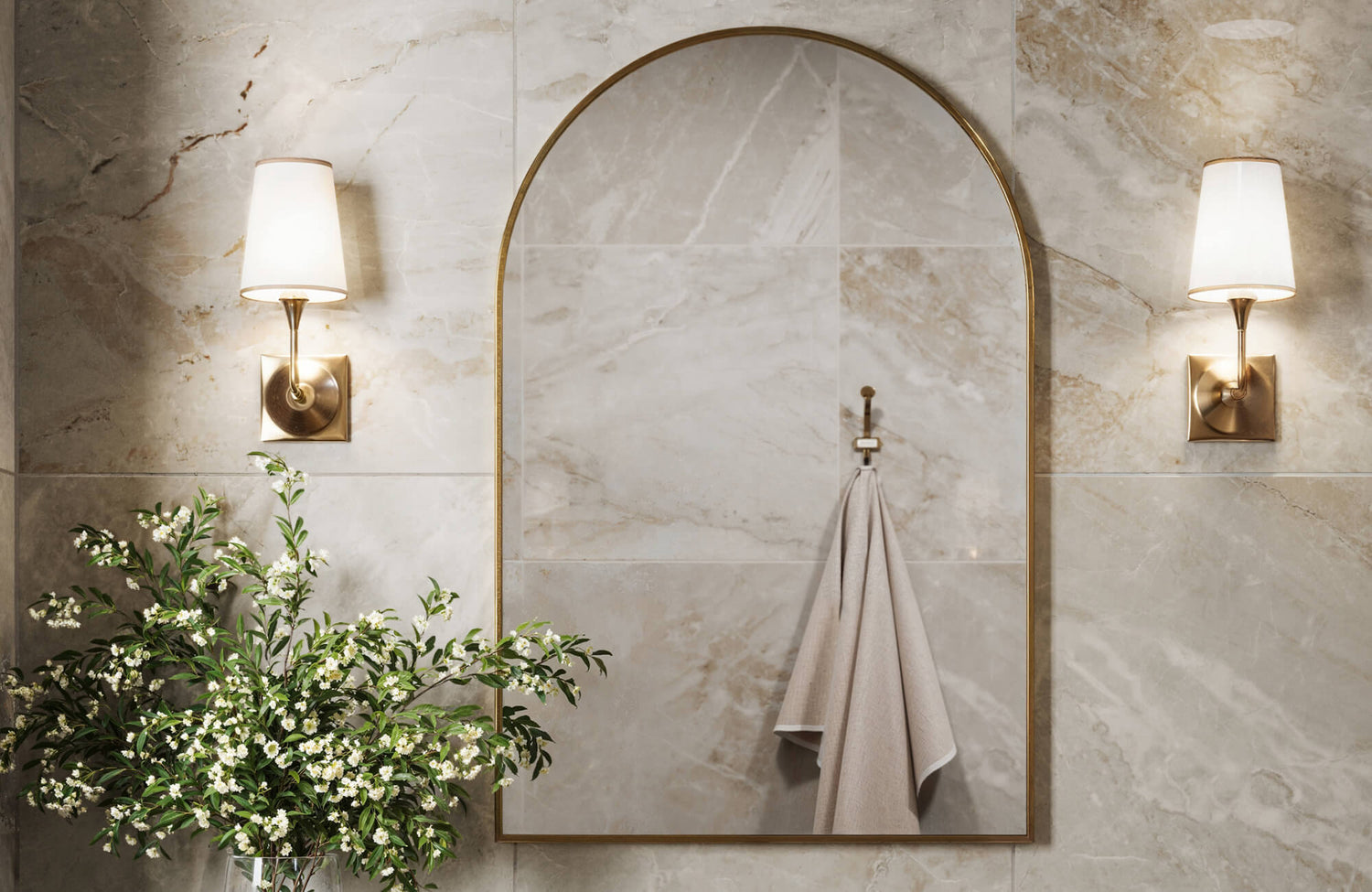 Arched mirror framed in brushed gold, reflecting warm lighting and set against polished marble-effect wall tiles.