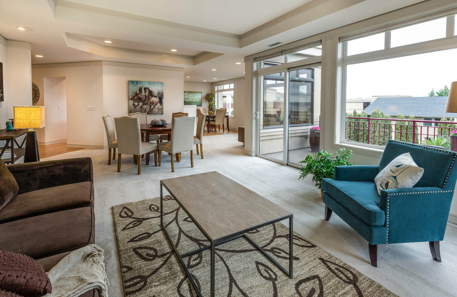 Bright open living room with patterned area rug, modern seating, dining space, and large windows opening to a balcony.