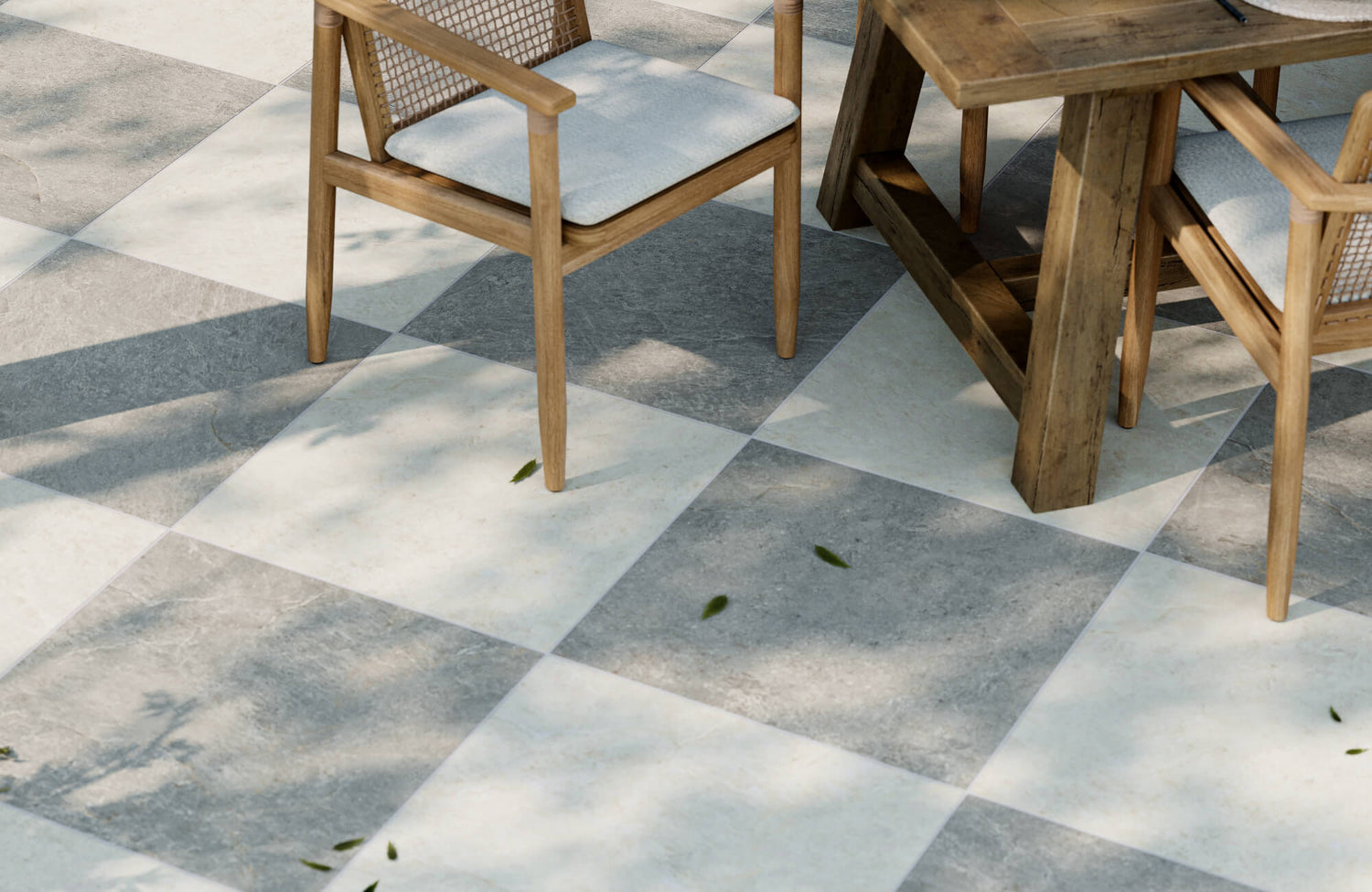 Outdoor dining area with wood furniture set on gray and white checkerboard porcelain paver tiles in a shaded patio space