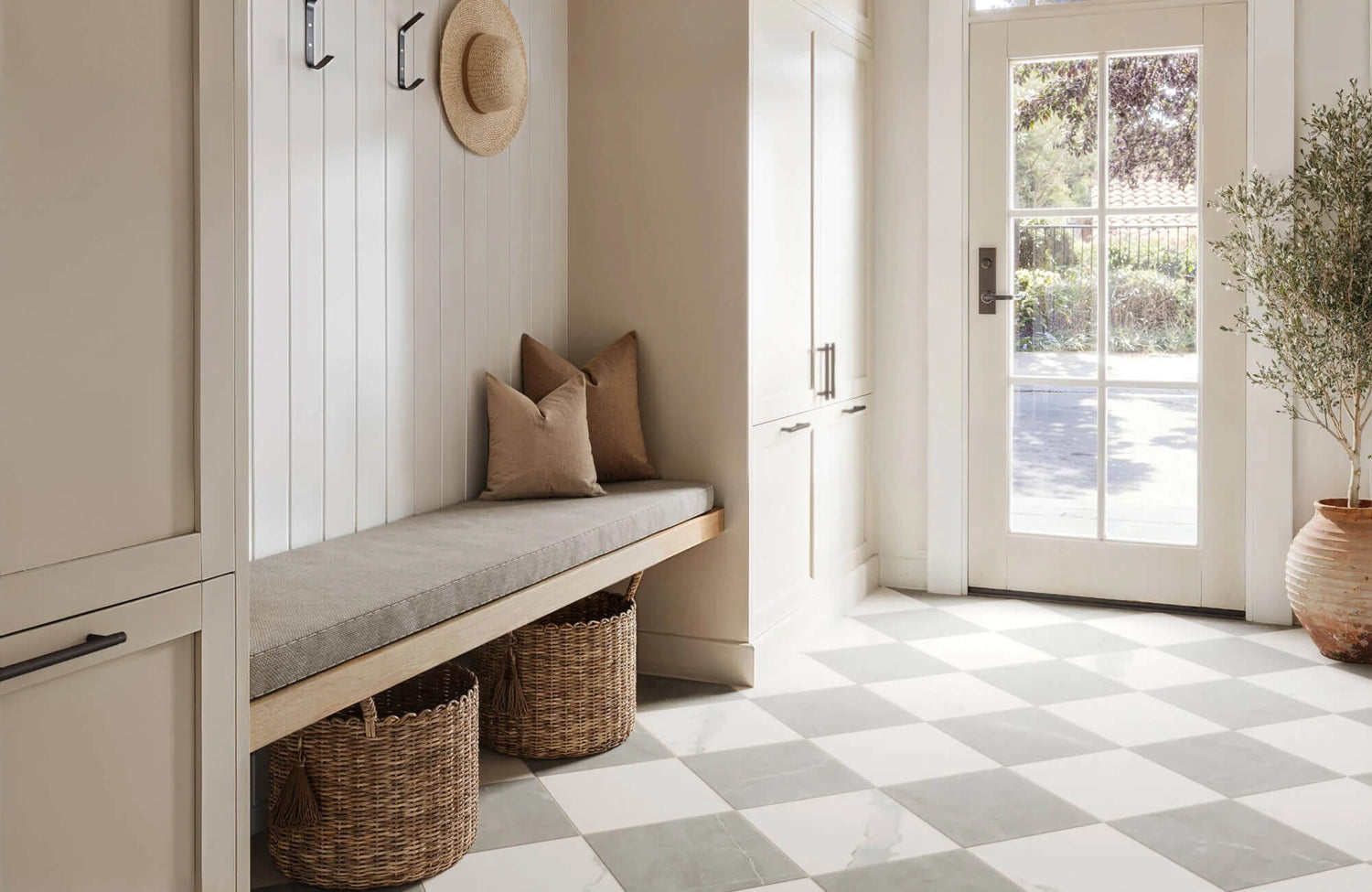 Bright entryway with sage and white checkered tile floor, built-in bench seating, woven baskets, and French door framed in soft neutrals.