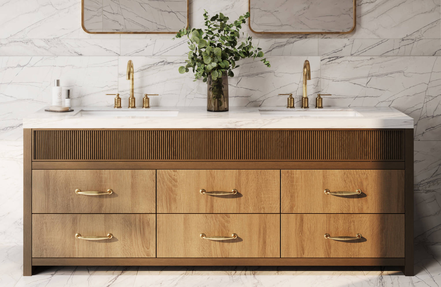 Elegant double vanity with gold fixtures and warm wood drawers set against polished white marble tile with grey veining.