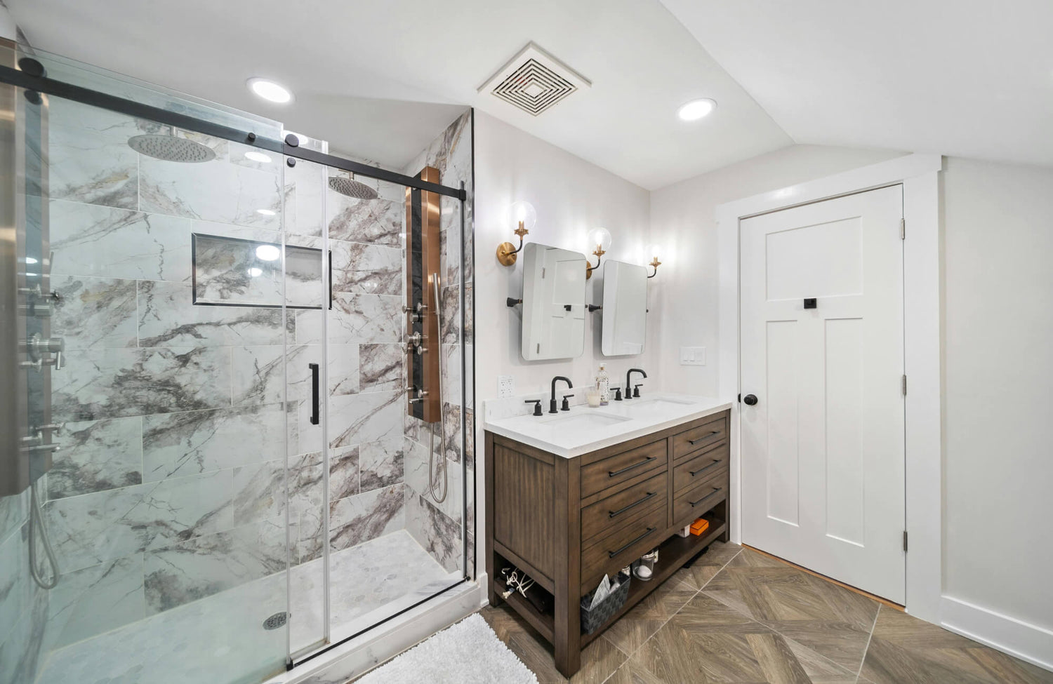 Modern bathroom featuring a freestanding double-sink vanity, frameless glass shower with marble tile, and warm wood-look flooring.