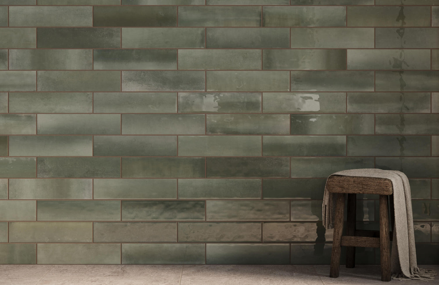 Glossy green subway tiles create a rich, earthy backdrop, paired with a rustic wooden stool draped with a neutral cloth.