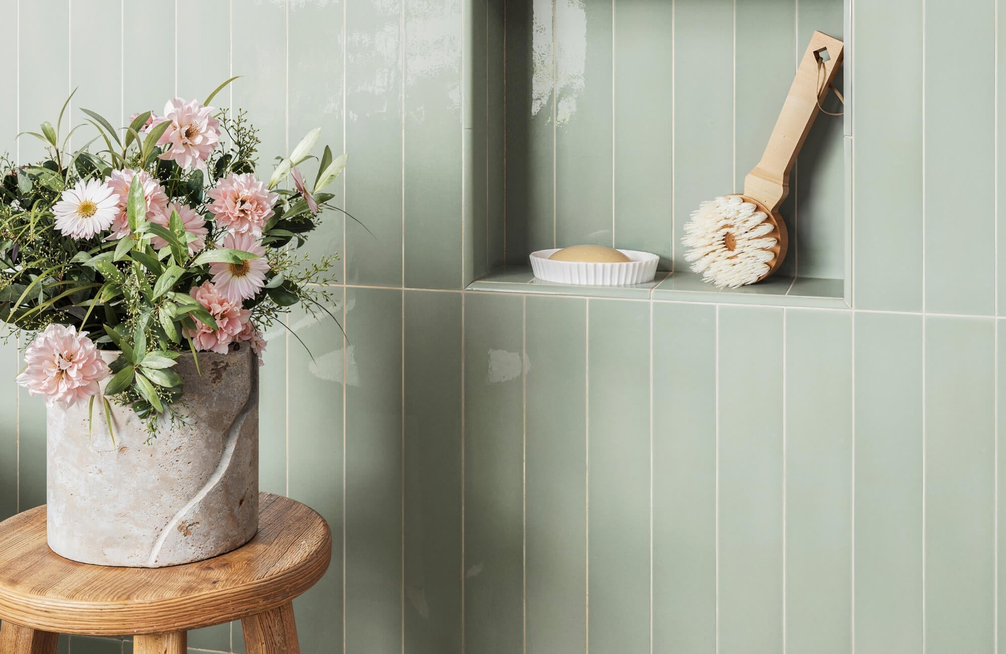 Soft sage green subway tiles line a shower wall and recessed shelf, paired with a wooden bath brush and simple soap dish for a clean, calming look.