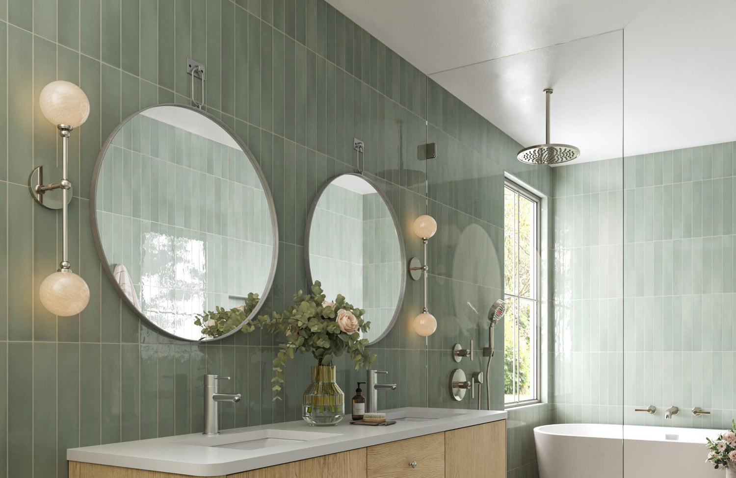 Modern bathroom with twin round mirrors, brushed metal fixtures, and vertical green tile backsplash, styled with florals and soft ambient lighting.
