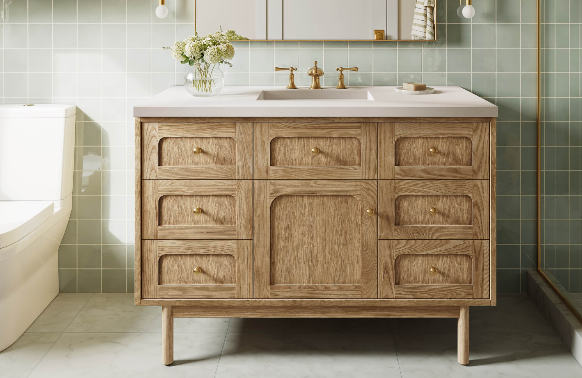 Modern bathroom with a natural light wood vanity, brass fixtures, and soft green tiled backsplash creating a warm, inviting space.