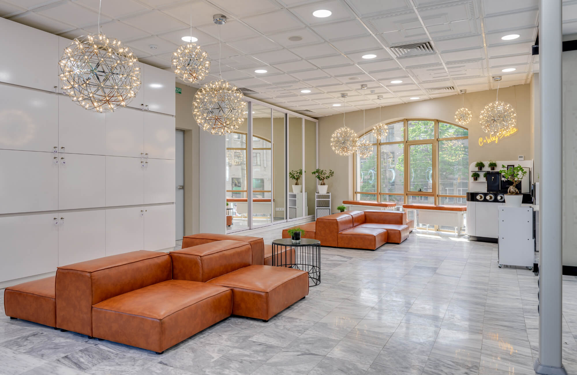 Modern lobby with brown leather modular seating, marble look tile flooring, globe pendant lights, and floor-to-ceiling windows.