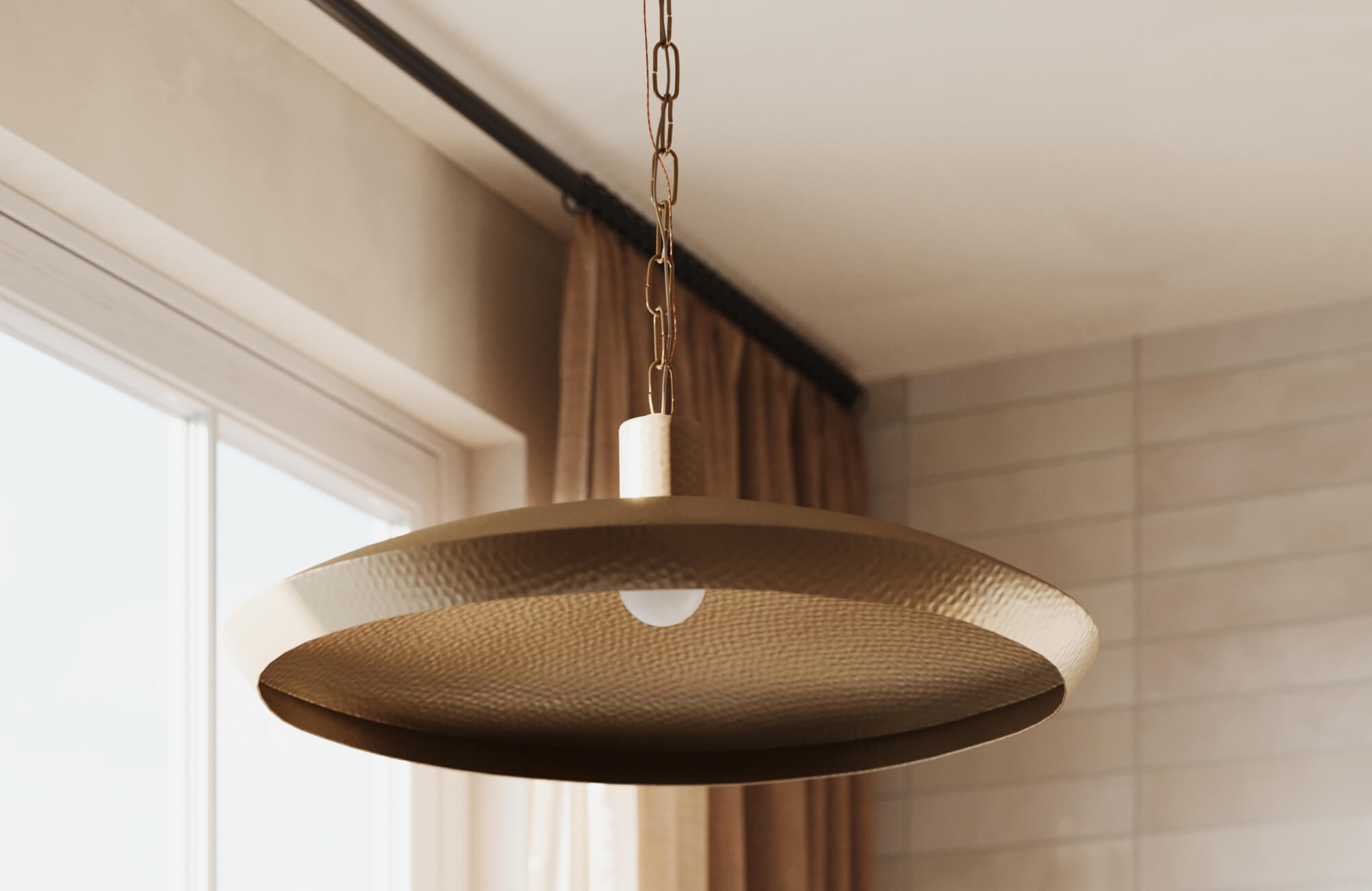 Sleek hammered brass pendant light with a wide, shallow dome shade suspended by a chain over neutral tile wall.