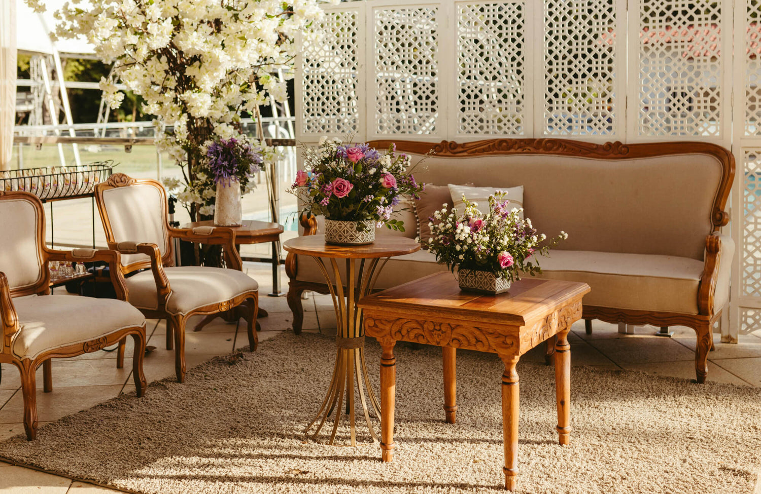 Elegant vintage-style seating area with carved wood furniture, floral arrangements, a polypropylene rug, and a white lattice privacy screen.