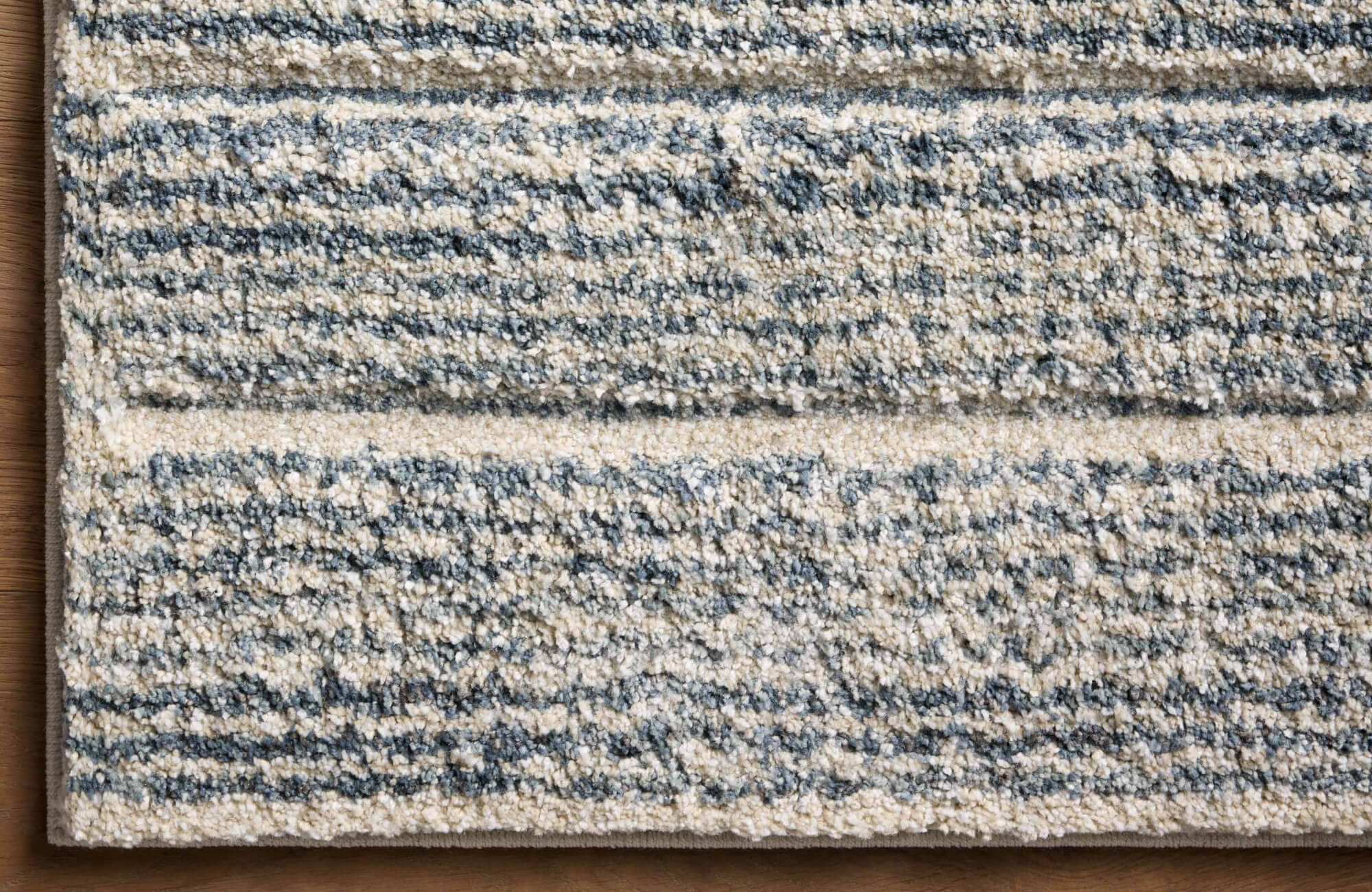 A low-pile polypropylene rug with textured linear patterns in soft neutral and blue tones, adding depth and warmth to any space.