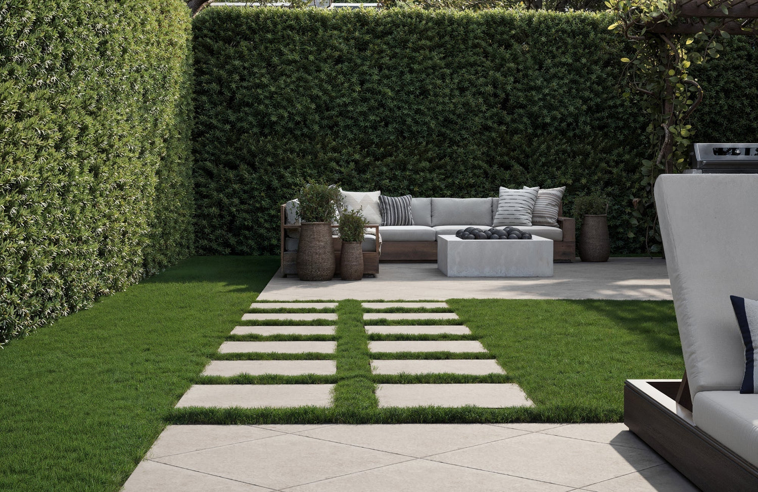 Modern backyard with porcelain paver walkway leading to a lounge area with neutral seating and a concrete fire pit surrounded by greenery.