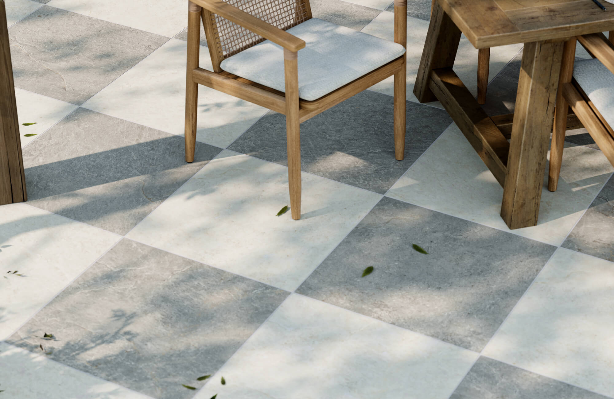 Checkerboard-pattern porcelain pavers in light and dark gray set beneath a rustic outdoor dining table and woven-back wood chairs.