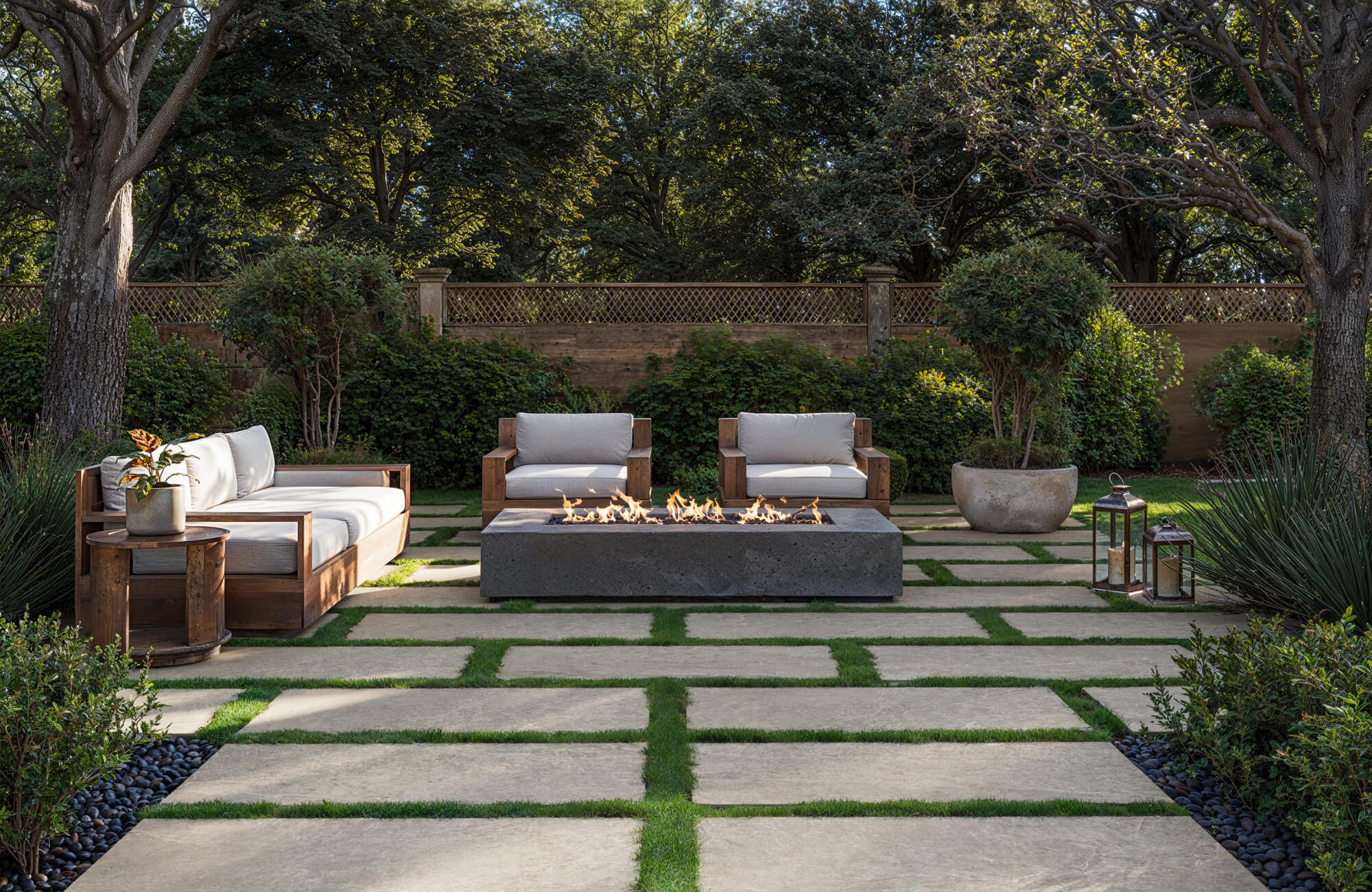 Modern outdoor patio with large beige porcelain pavers set in grass, surrounding a sleek concrete fire pit and wooden lounge seating.