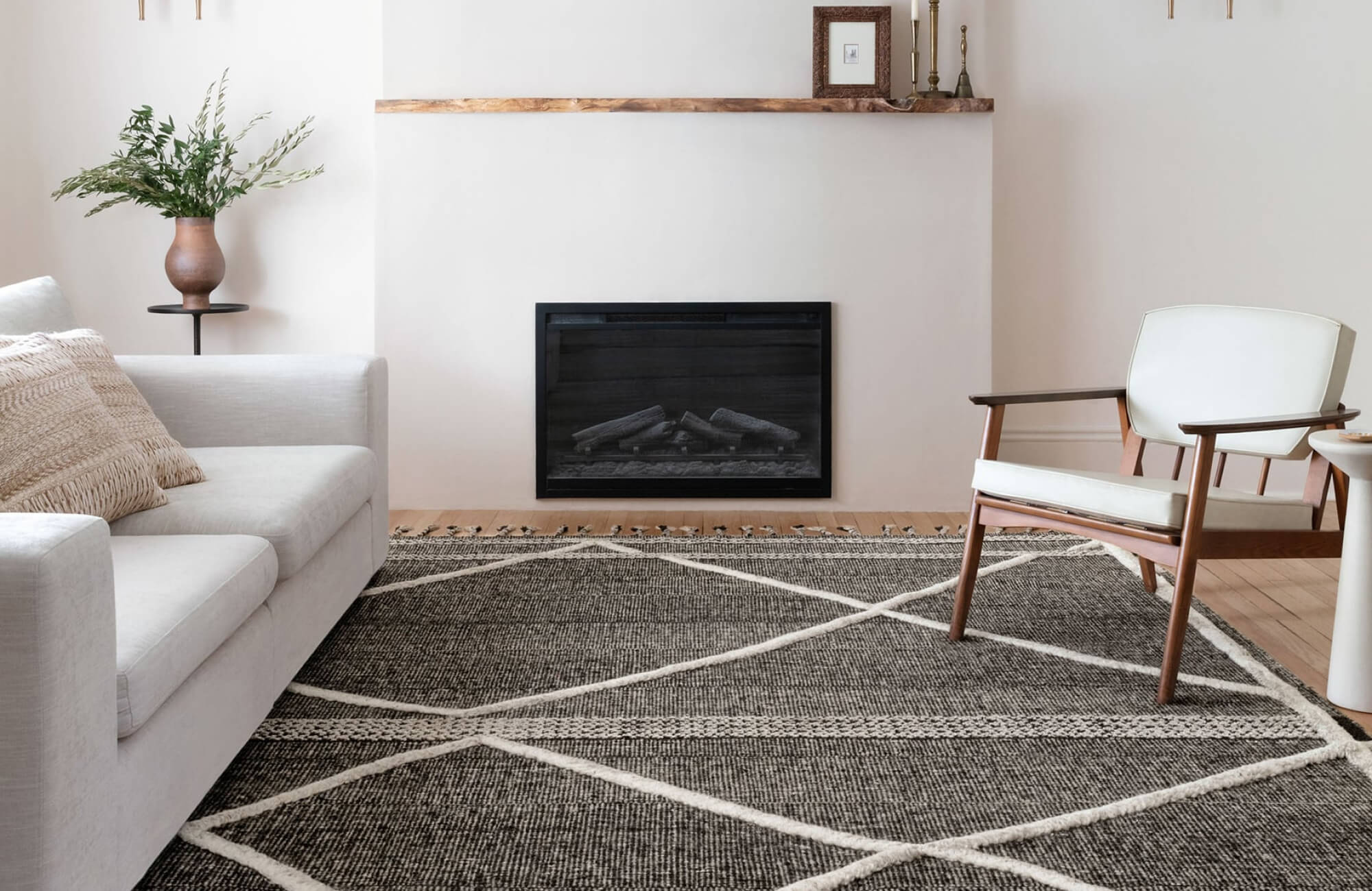 A modern living room with a neutral palette, featuring a black and white geometric rug, a sleek fireplace, a white sofa with textured pillows, and a mid-century wooden armchair.