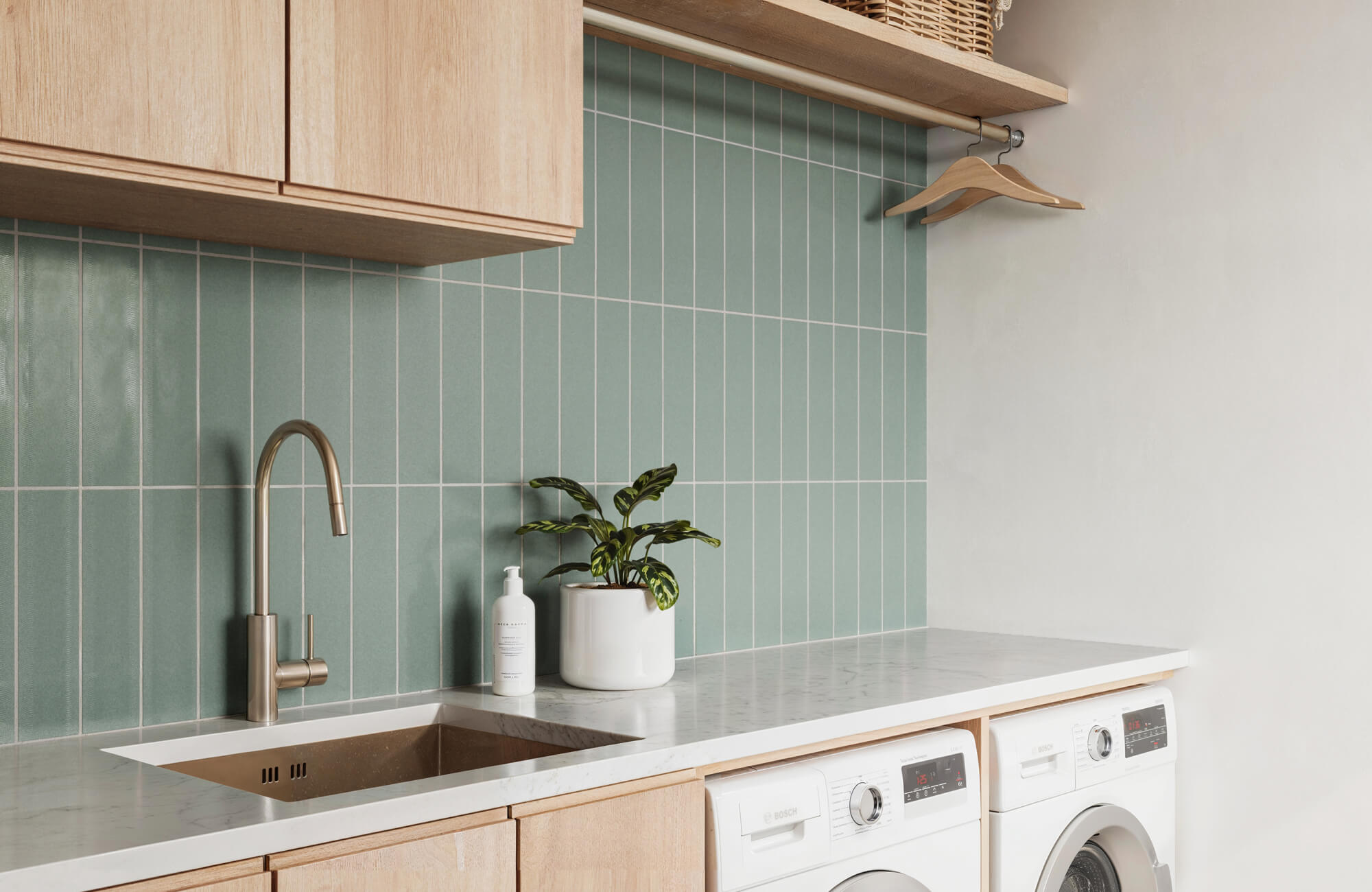Minimalist laundry room featuring mint green vertical subway tile backsplash, wooden cabinetry, and sleek white appliances.