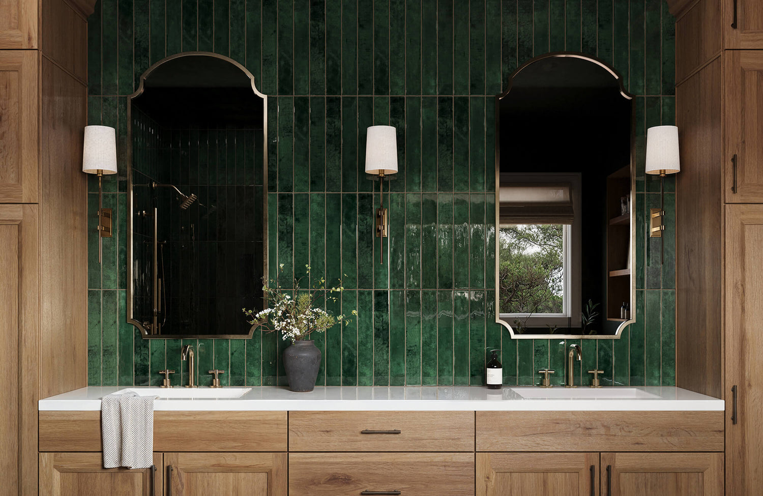 Modern bathroom with dual sinks, green vertical subway tiles, arched mirrors, wood cabinetry, and brass fixtures.