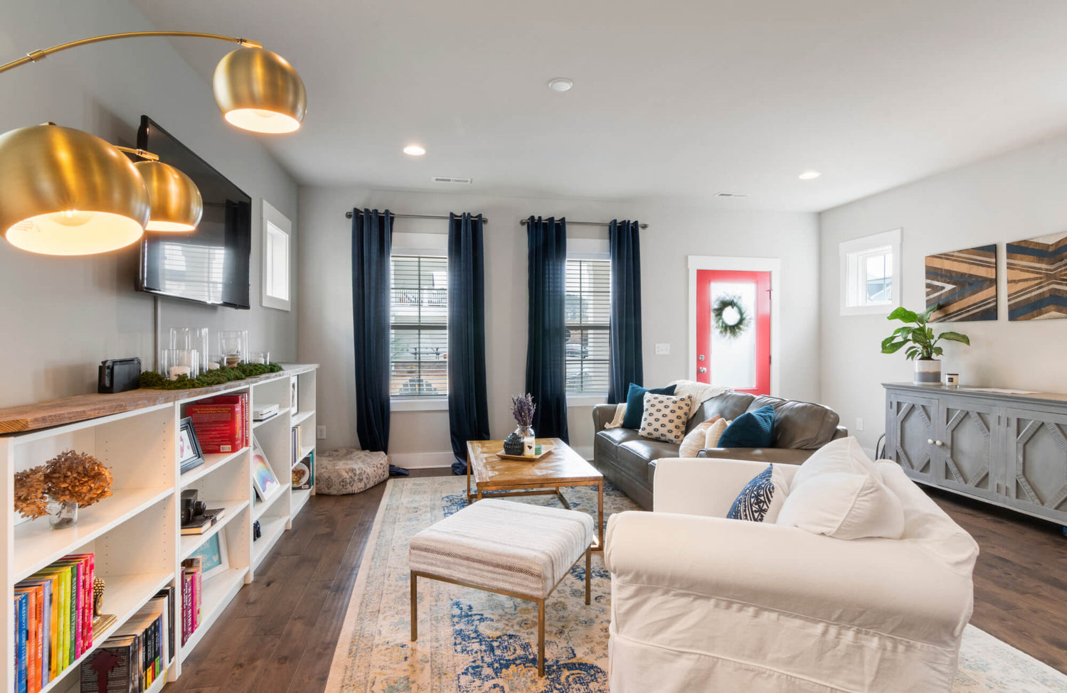 Bright, modern living room with a traditional rug, leather sofa, white armchair, navy curtains, and a red front door.