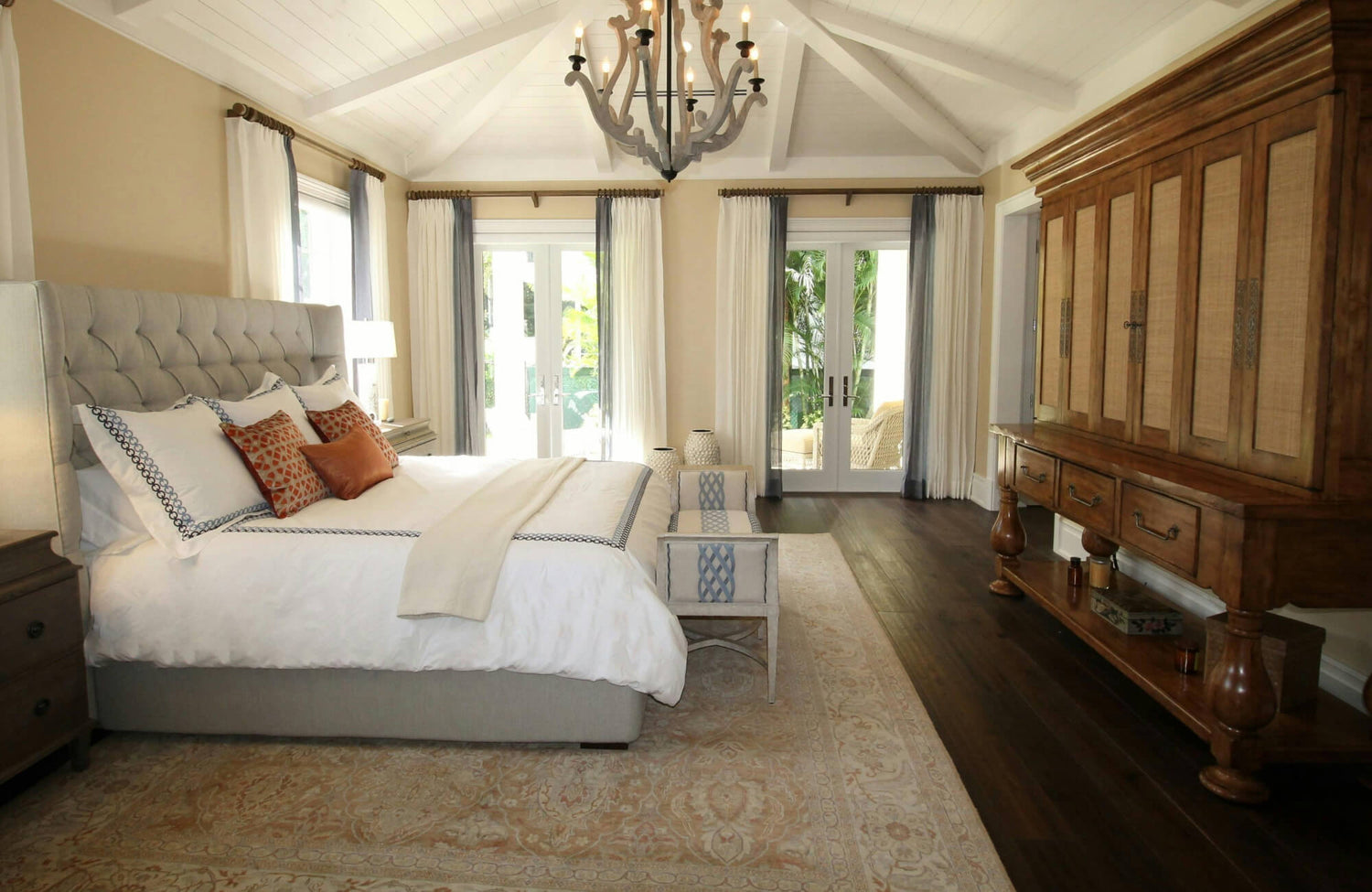 Elegant bedroom with a wool rug, a tufted upholstered bed, warm wood furnishings, and large windows opening to a lush garden view.