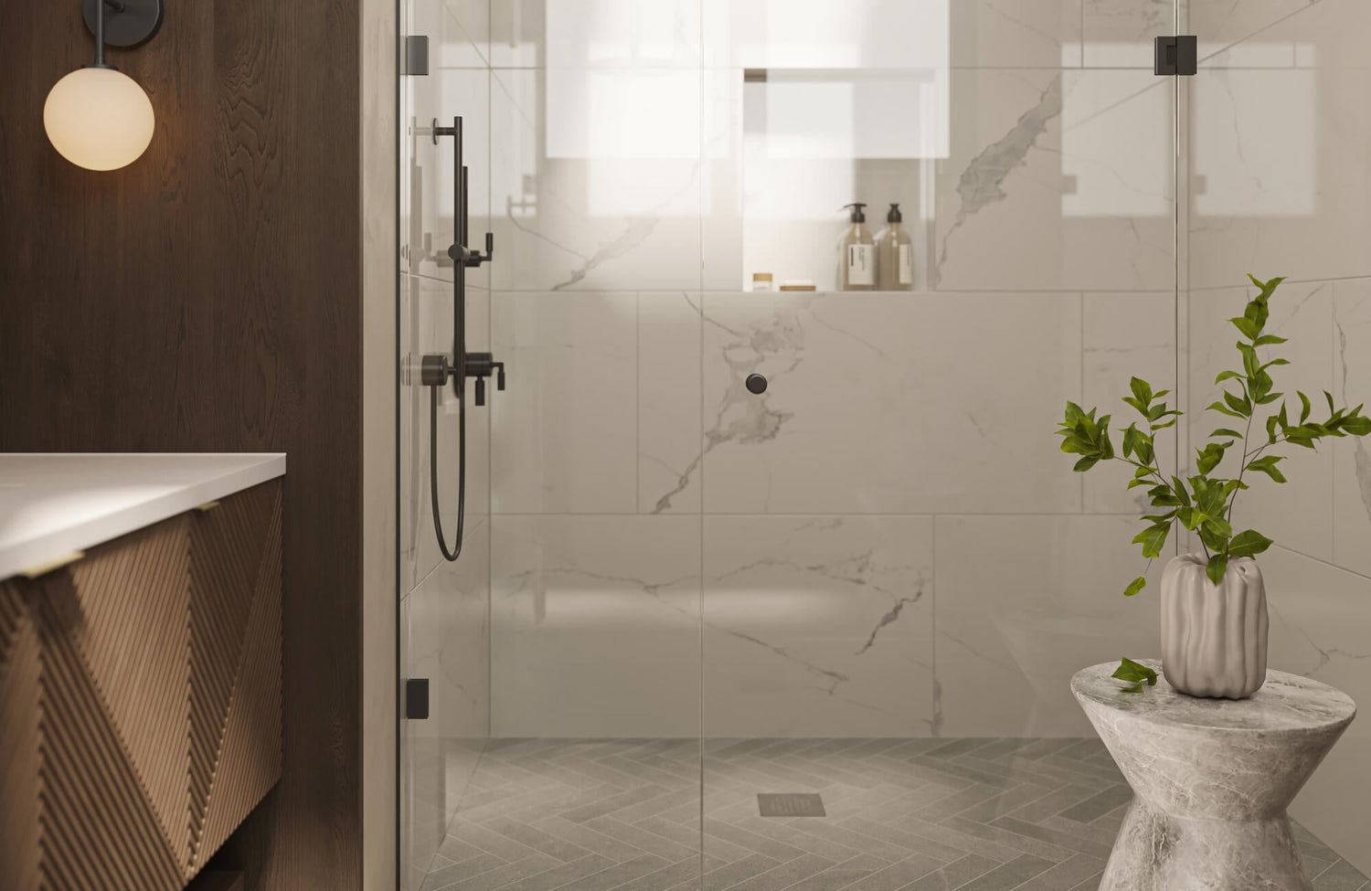 This serene bathroom design trend features a frameless glass shower with marble-look wall tiles, a herringbone tile shower floor, matte black fixtures, and warm wood vanity cabinetry for a spa-inspired, modern aesthetic.