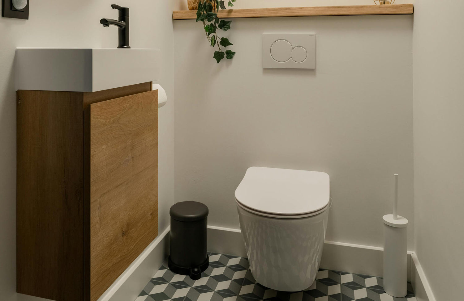 A modern small bathroom vanity with a wood-front cabinet and compact rectangular sink sits beside a sleek wall-mounted toilet, geometric floor tiles, and minimal accessories that create a clean, space-efficient look.