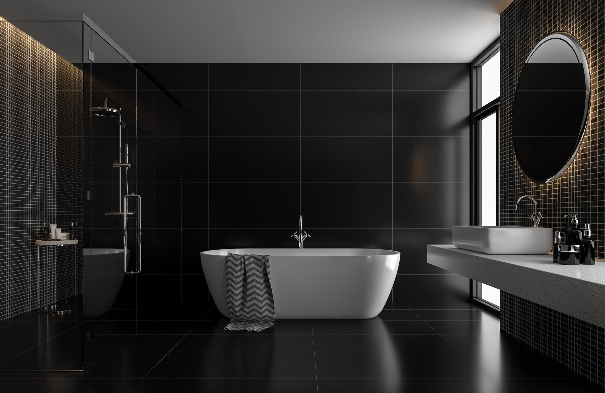 Modern bathroom with black wall and floor tiles, a freestanding white tub, floating vanity, and backlit round mirror near a window.