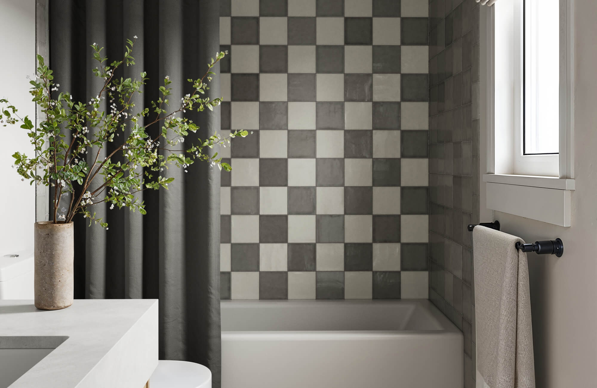 Modern bathroom with elegant gray and white checkered tiles on the wall, complemented by a sleek white bathtub and minimalist decor.