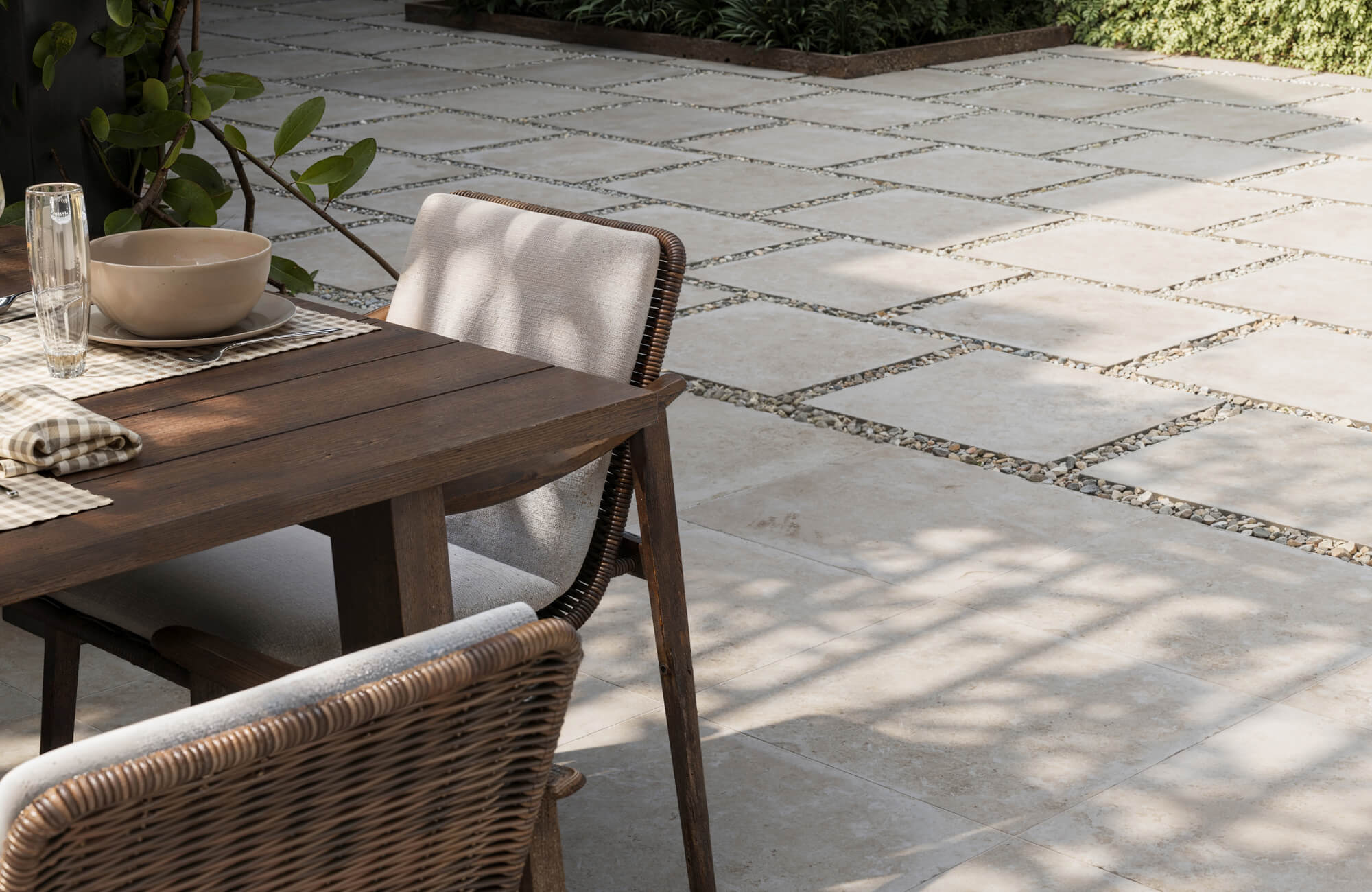 Neutral stone-look pavers arranged in a grid with gravel joints, creating a modern patio beside a wooden dining set.