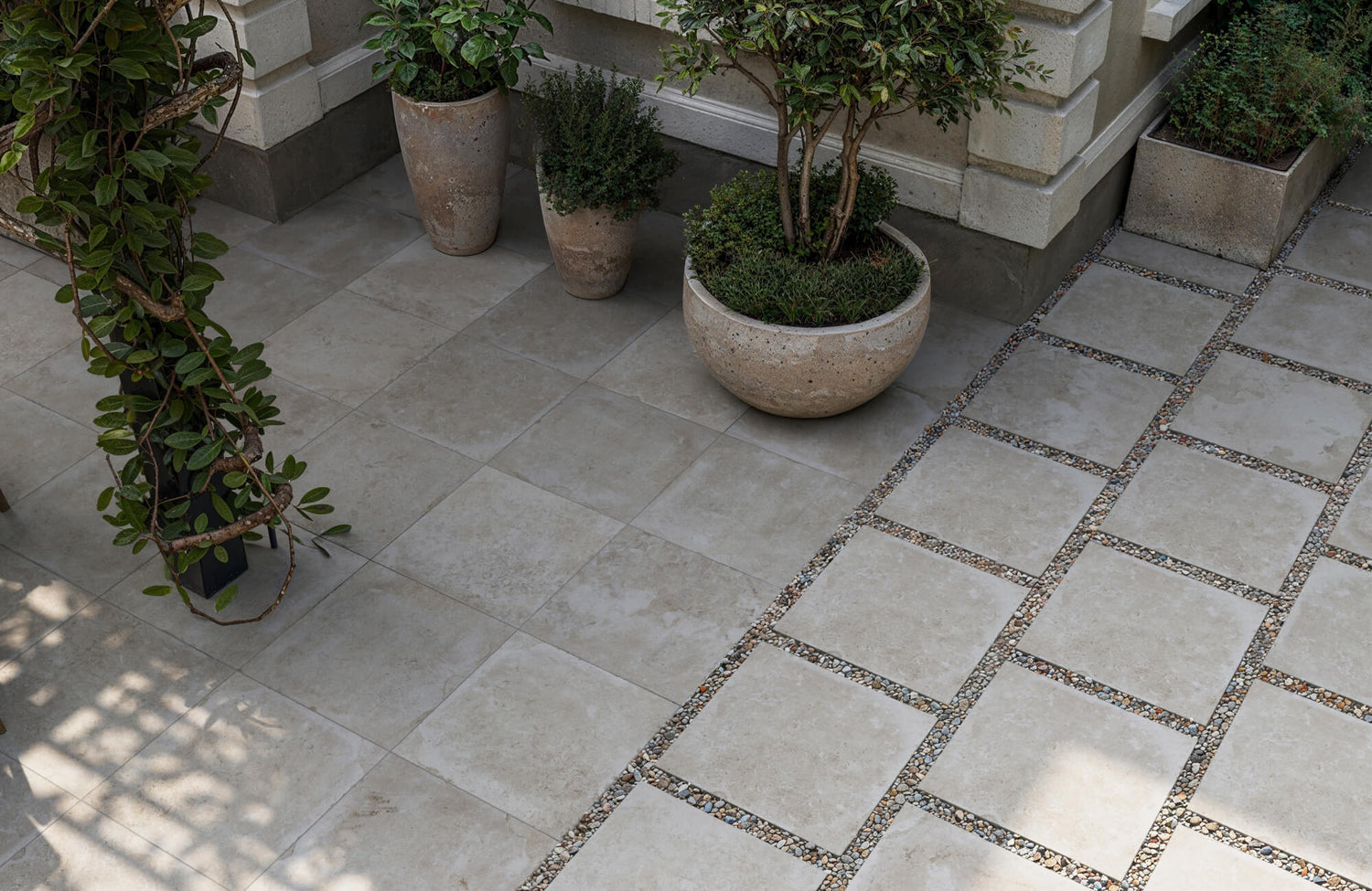 Neutral-toned porcelain tiles used as pavers in a refined outdoor setting, accented with gravel joints and elegant concrete planters