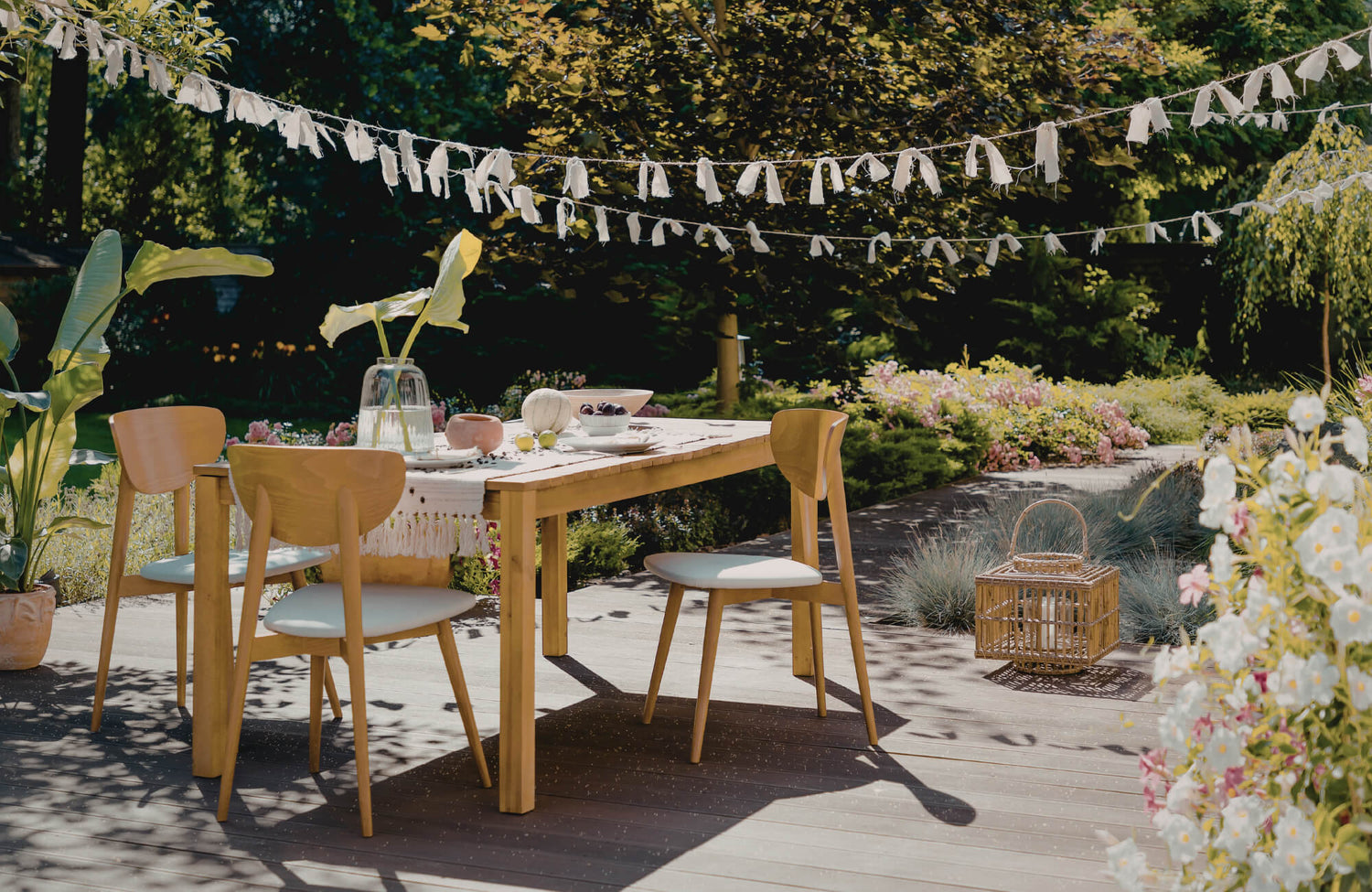 Outdoor wooden dining table with cushioned chairs on a garden deck, styled for relaxed dining and casual lounge-style entertaining.