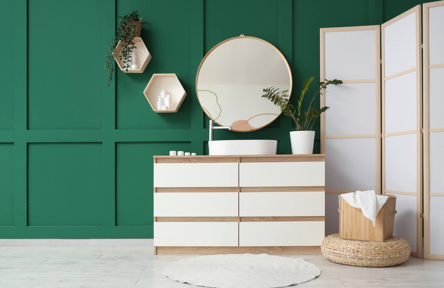 Minimalist bathroom with green paneled wall, round wood-framed mirror, white vanity, potted plant, and modern natural accents.