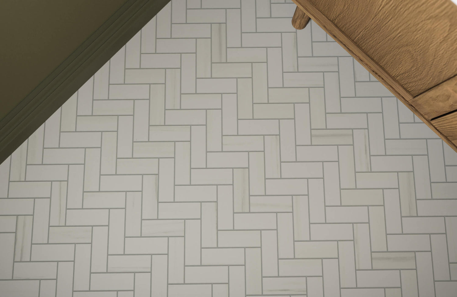 White herringbone tile floor with subtle gray veining, creating a clean and structured pattern beneath wood cabinetry.
