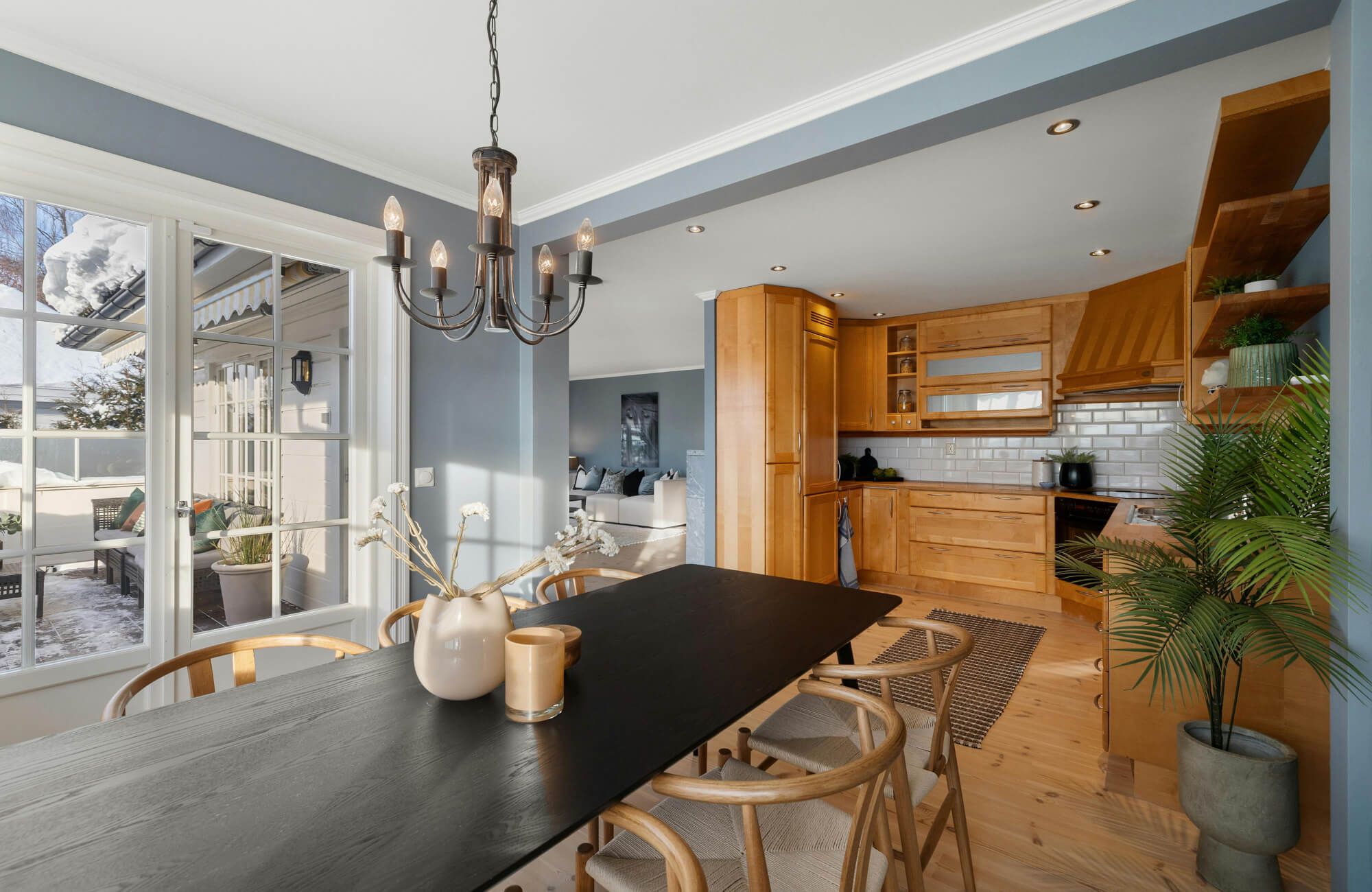 Rustic dining room with a black wood table, curved chairs, and an industrial chandelier featuring candle-style bulbs and metal arms.