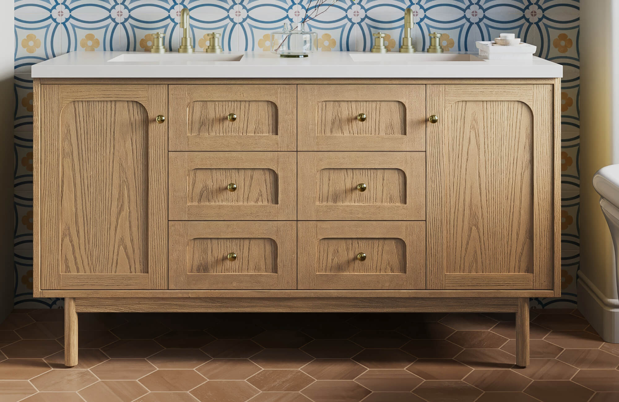 Light oak vanity with brass hardware set against floral blue-and-gold tiles and matte terracotta hexagon flooring.