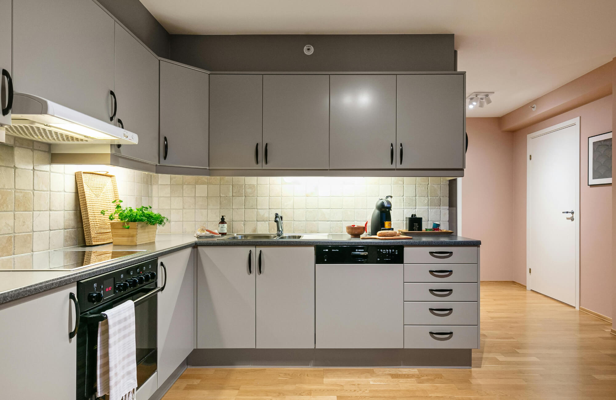 Modern kitchen with gray cabinets, black appliances, and a beige square-tile backsplash above the sink and countertop.