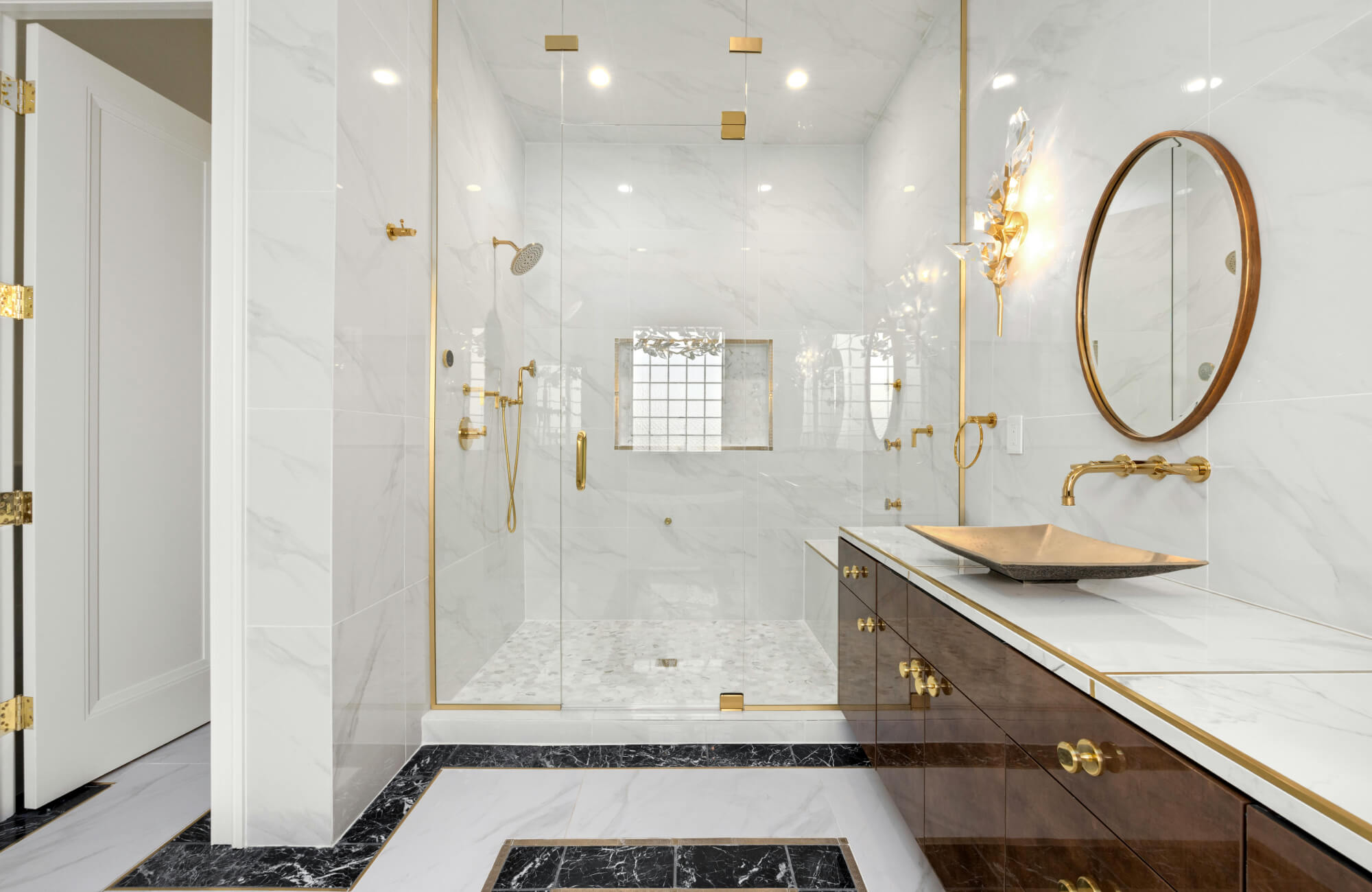 Luxury marble bathroom with Carrara-style wall tiles, glass shower enclosure, gold fixtures, and double vanity creating a bright spa-like space.