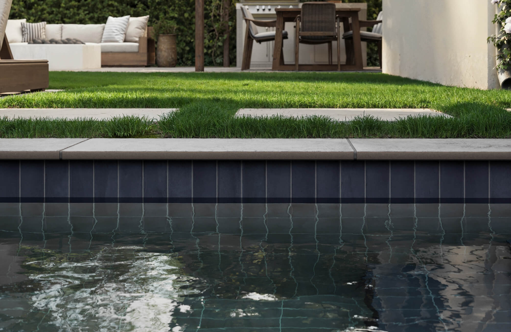 Sleek porcelain blue pool tiles add modern contrast to lush greenery and stone pavers in this serene backyard oasis.