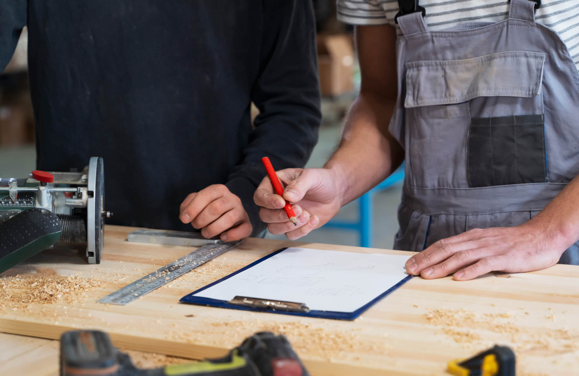 Two contractors review measurements and mark plans at a workbench with tools and wood shavings, highlighting the careful planning and craftsmanship involved in a professional bathroom renovation project.