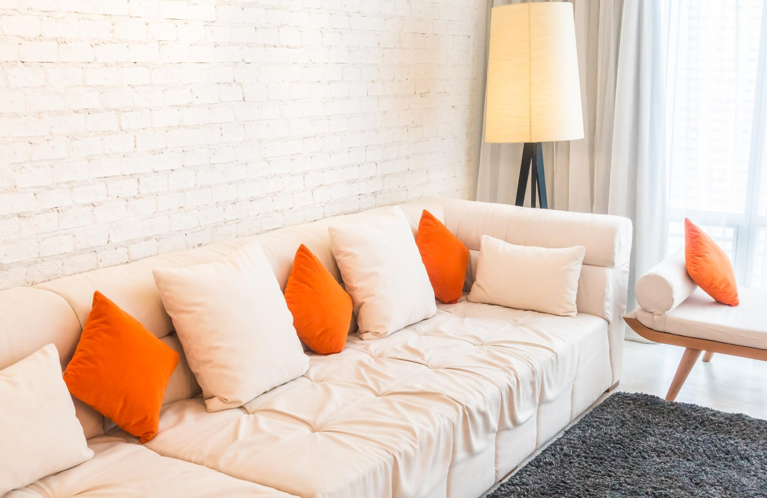 Decorative pillow in vibrant orange velvet and soft beige fabric arranged on a modern cream sofa, adding bold contrast and layered comfort to a bright, minimalist living room setting.