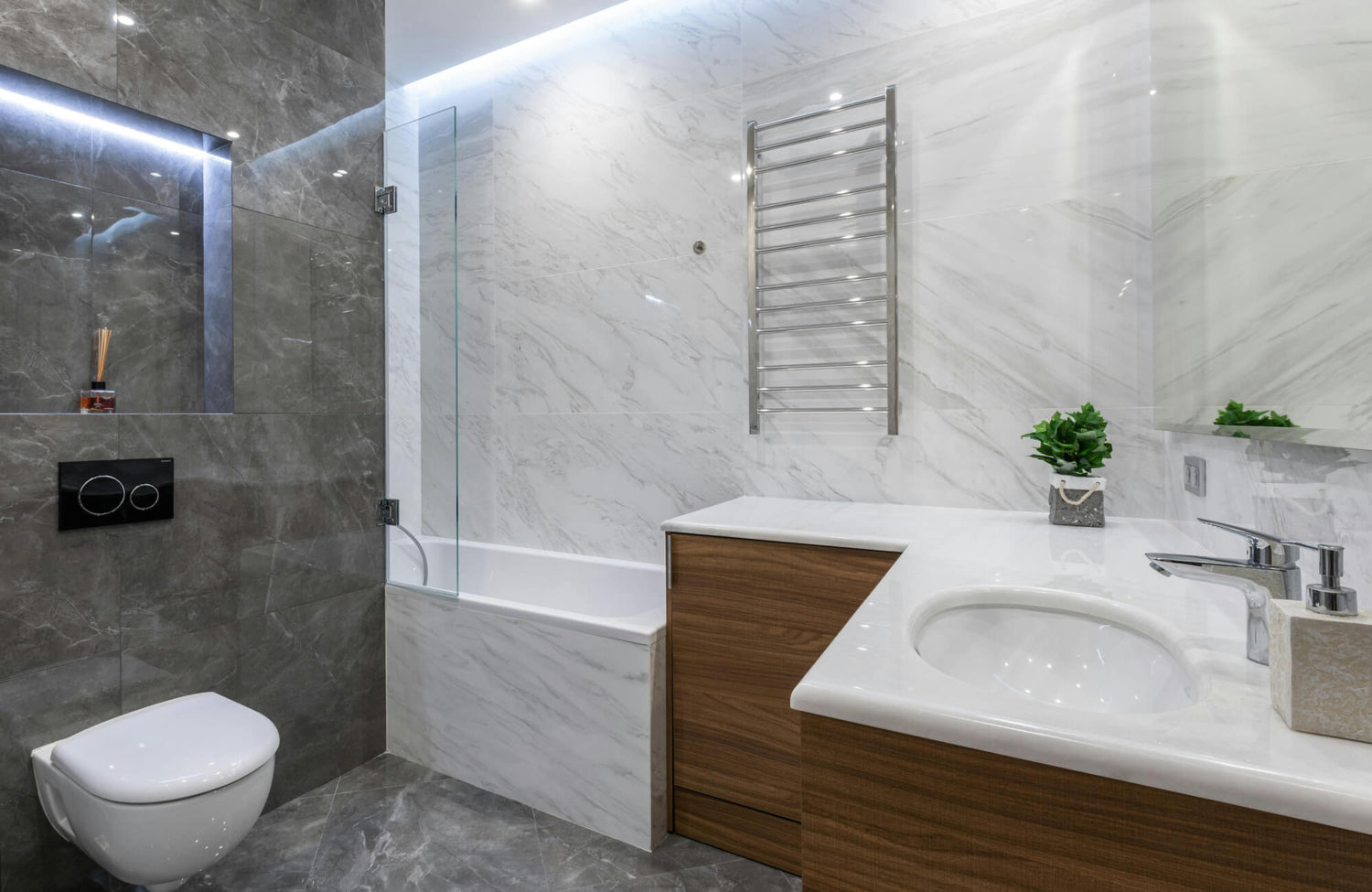 Modern corner vanity with wood finish, white countertop, and built-in sink, blending into a marble and gray tiled bathroom.