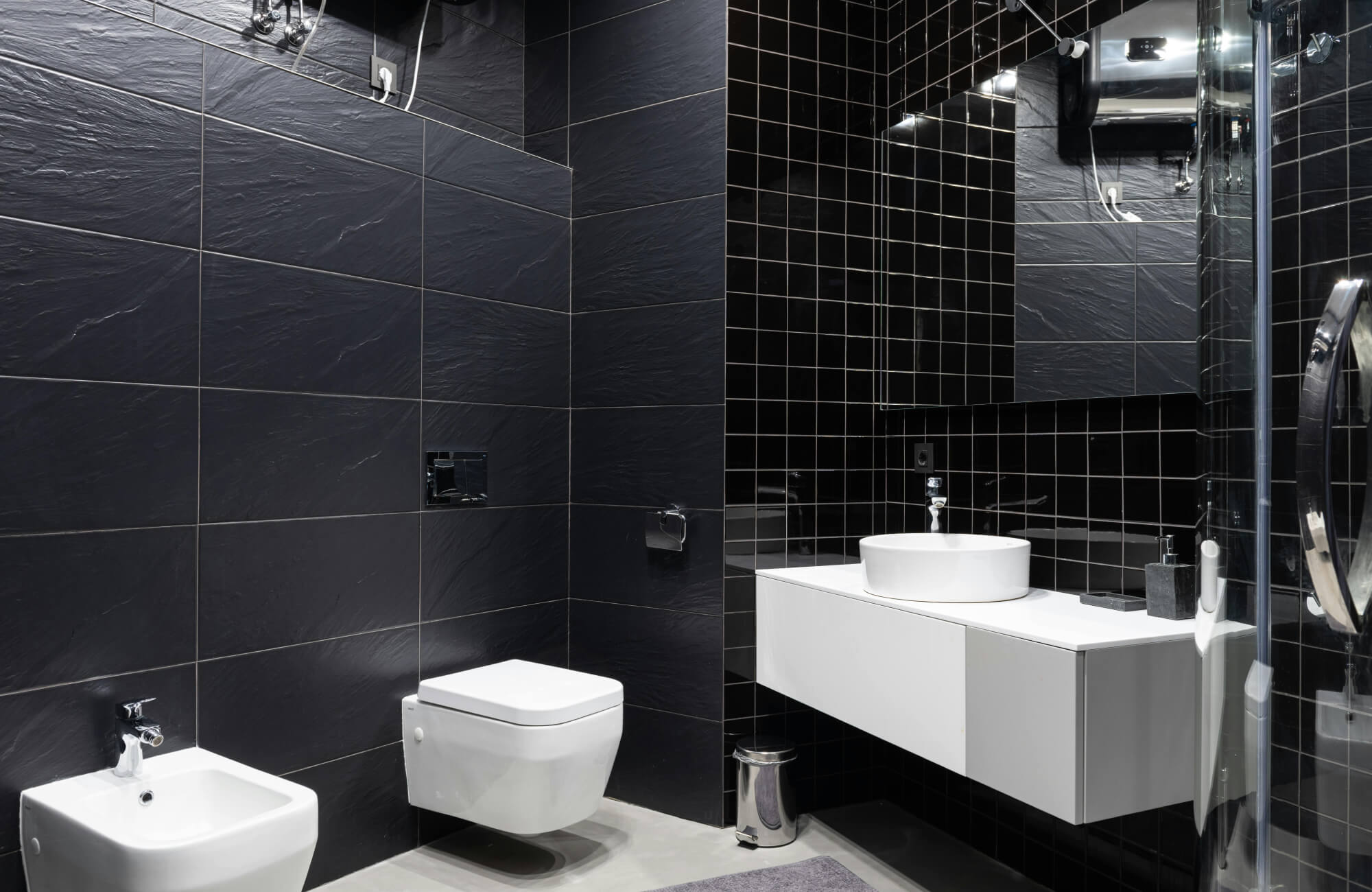 Modern bathroom with large-format black wall tiles and matte black fixtures, showcasing tile texture and contrast.