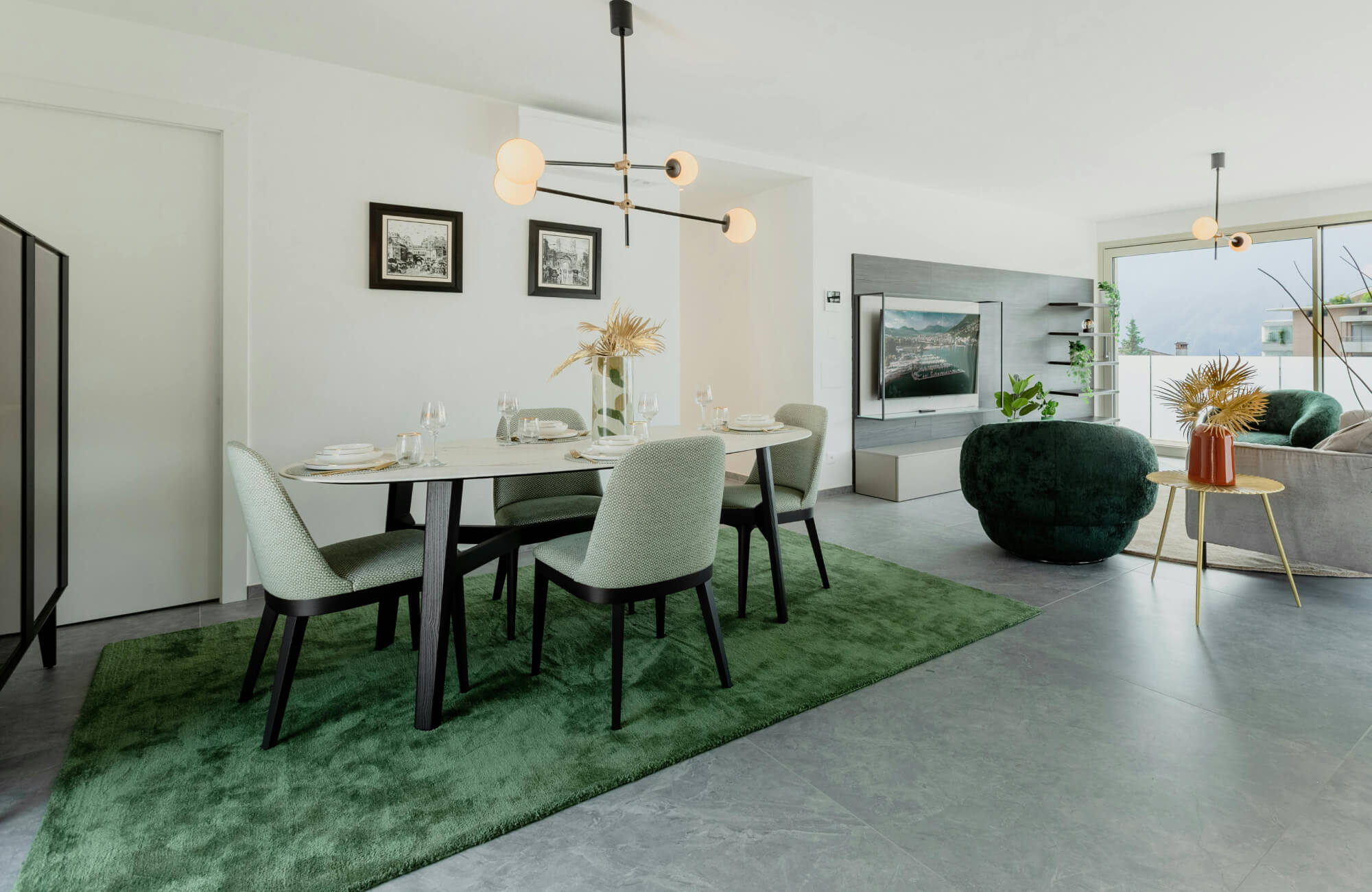 Modern open-concept dining and living space featuring a bold green rug, minimalist furniture, a globe chandelier, and stone-look flooring.