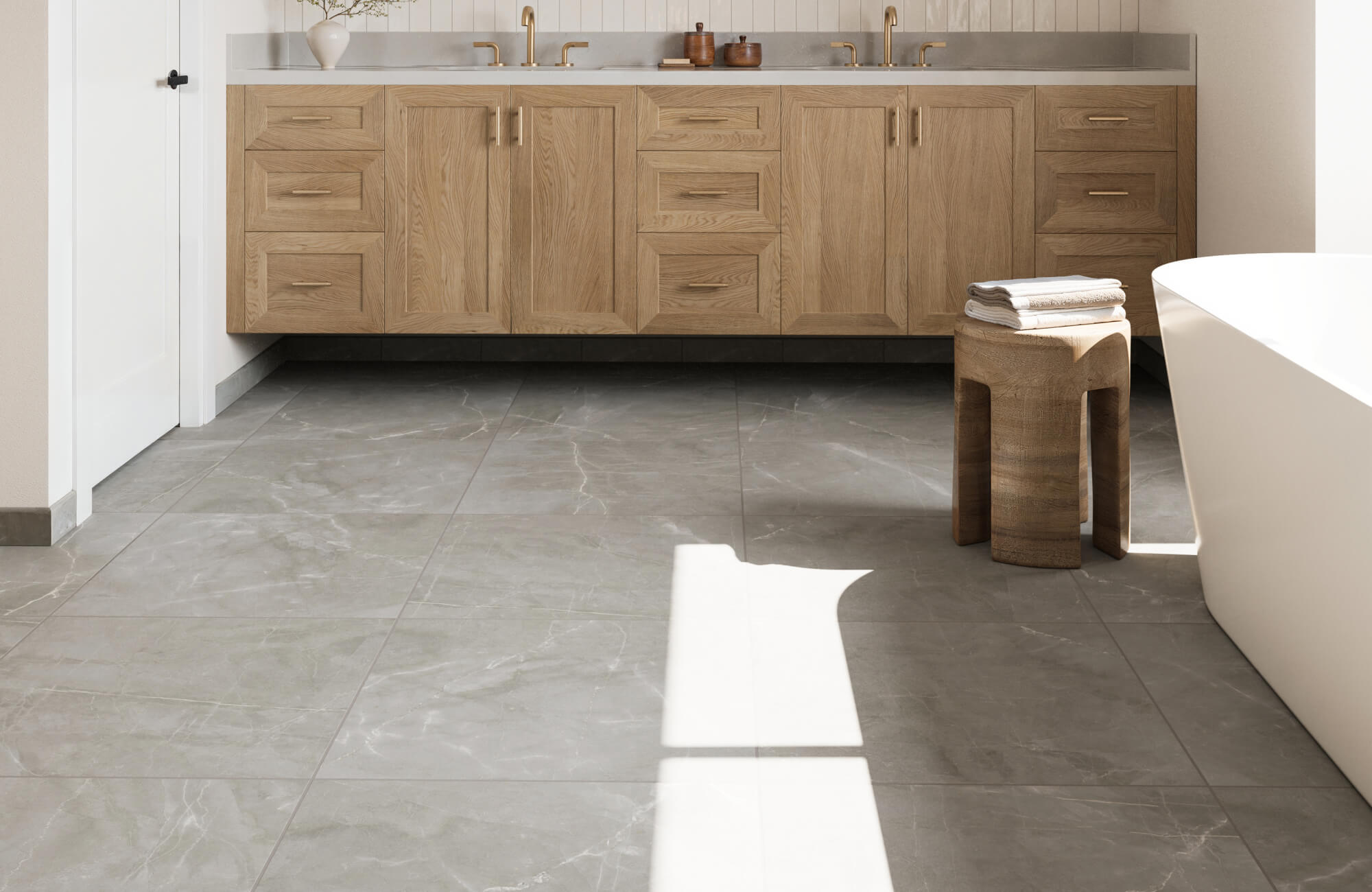 Spacious bathroom with gray marble look floor tiles and a light oak vanity with brass fixtures.