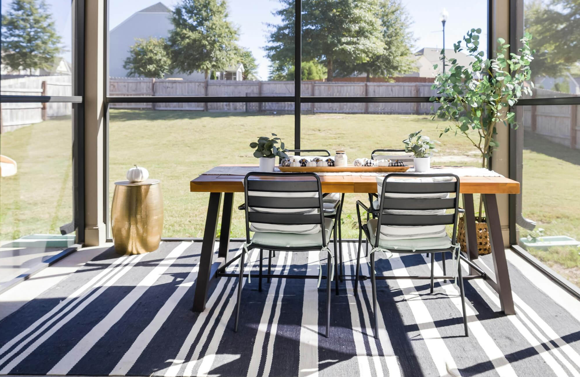 Chic patio dining area with a striped polypropylene rug, wooden table, and metal chairs, basking in the sunlight.