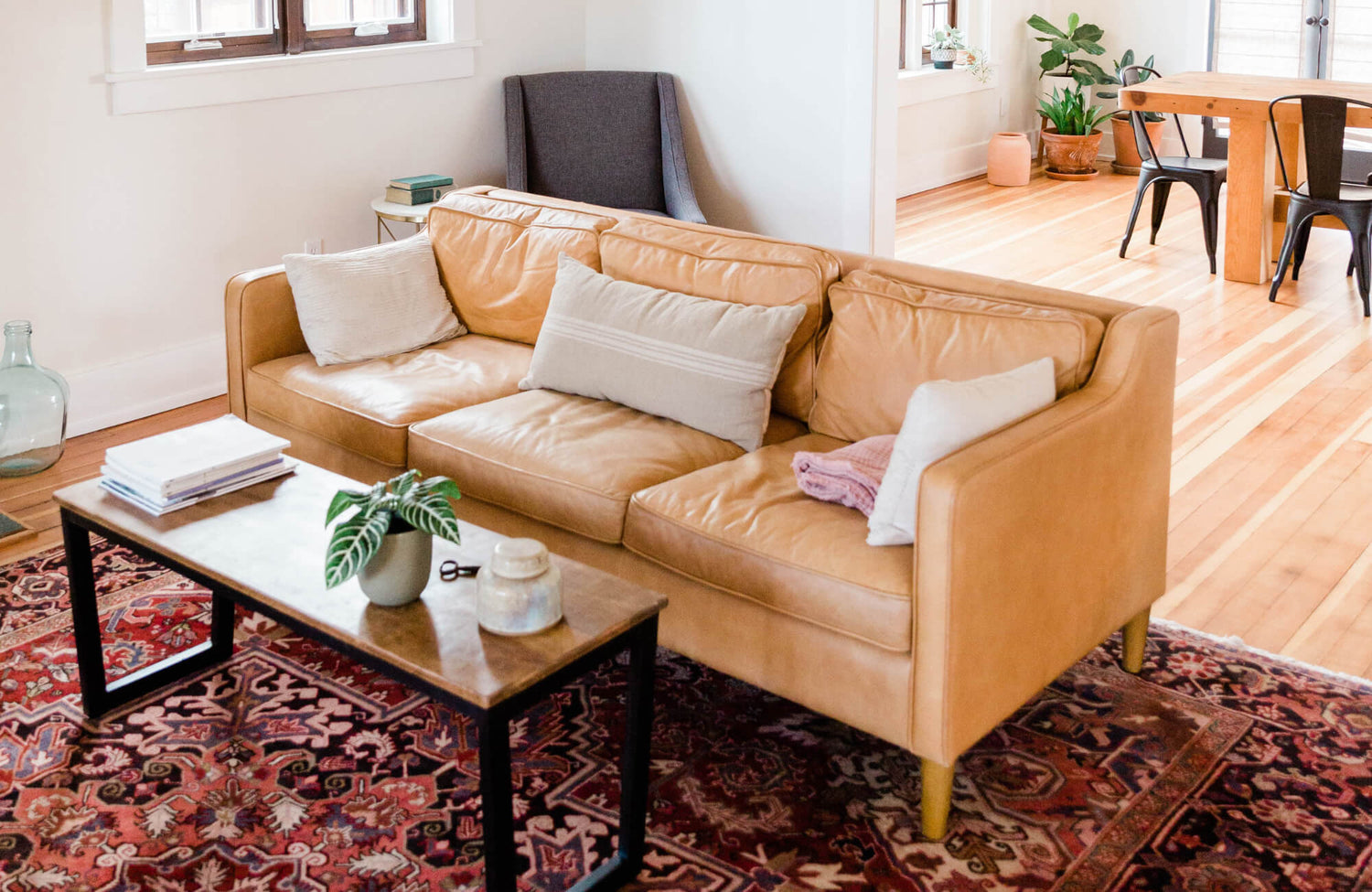 Warm-toned modern living room with a camel leather sofa, dark wood coffee table, and a richly patterned traditional red Persian rug.