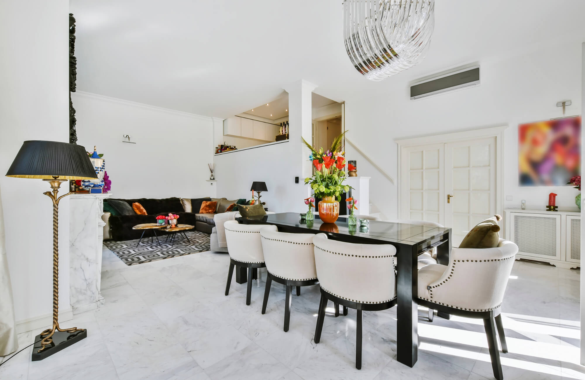 Modern dining and living room with marble tile flooring, black dining table, upholstered chairs, and decorative accents.