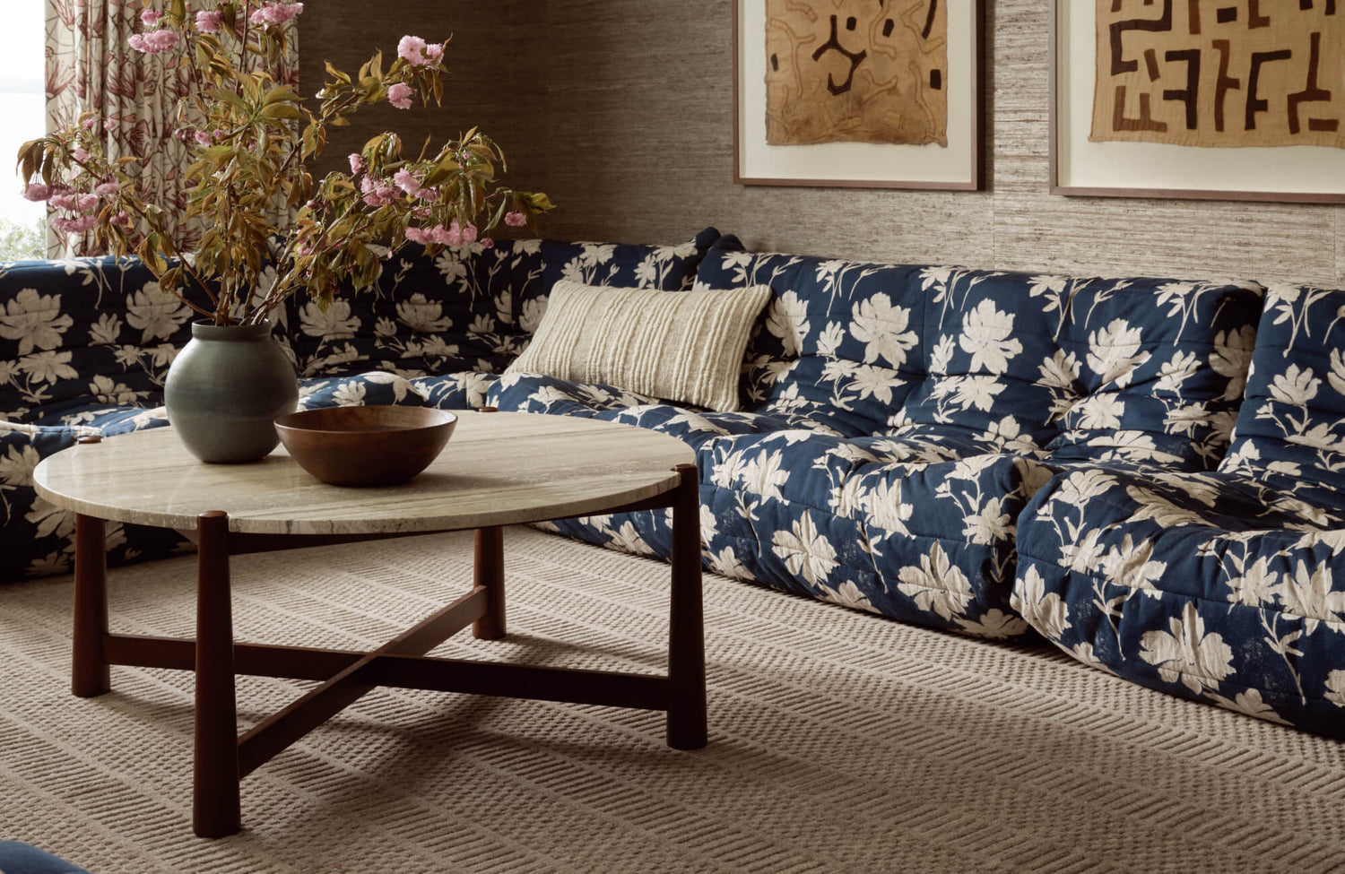 Plush sectional sofa in navy with bold white floral print, paired with a round travertine coffee table on a textured beige rug.